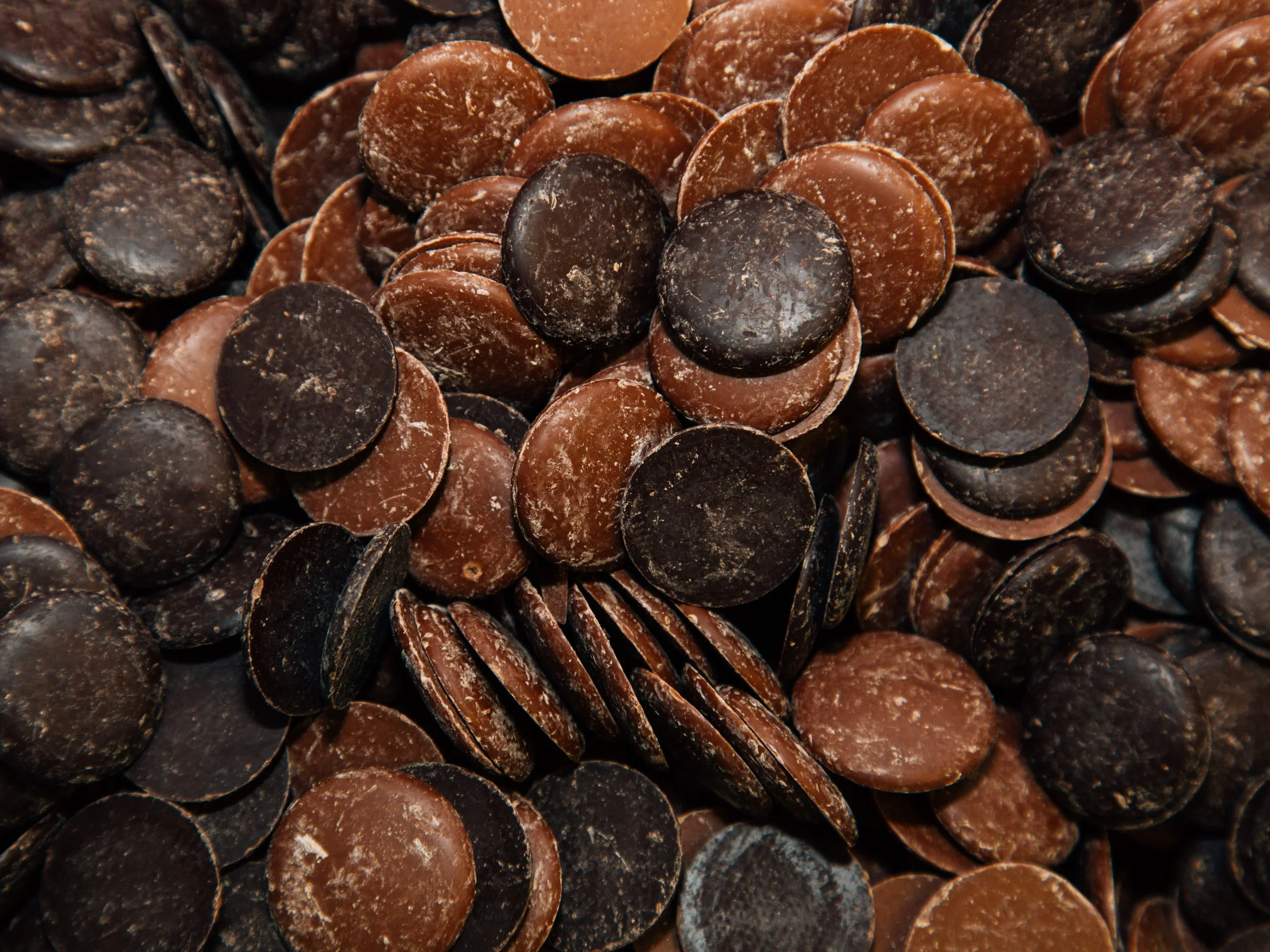 A pile of assorted chocolate chips in various sizes and shades of brown and black.