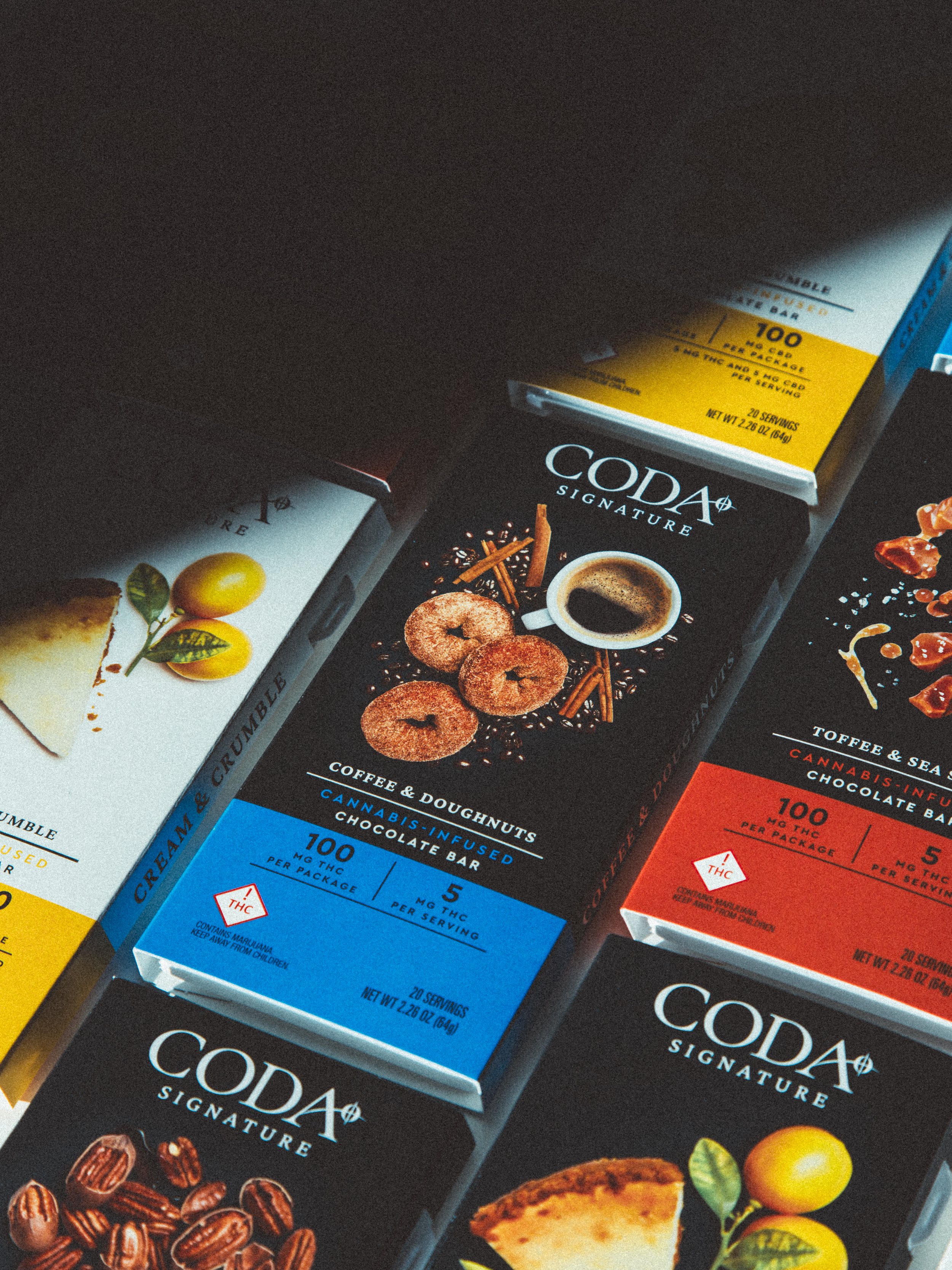 Assorted CBD edible boxes including coffee and doughnuts, chocolate bars, and other flavored treats in colorful packaging.