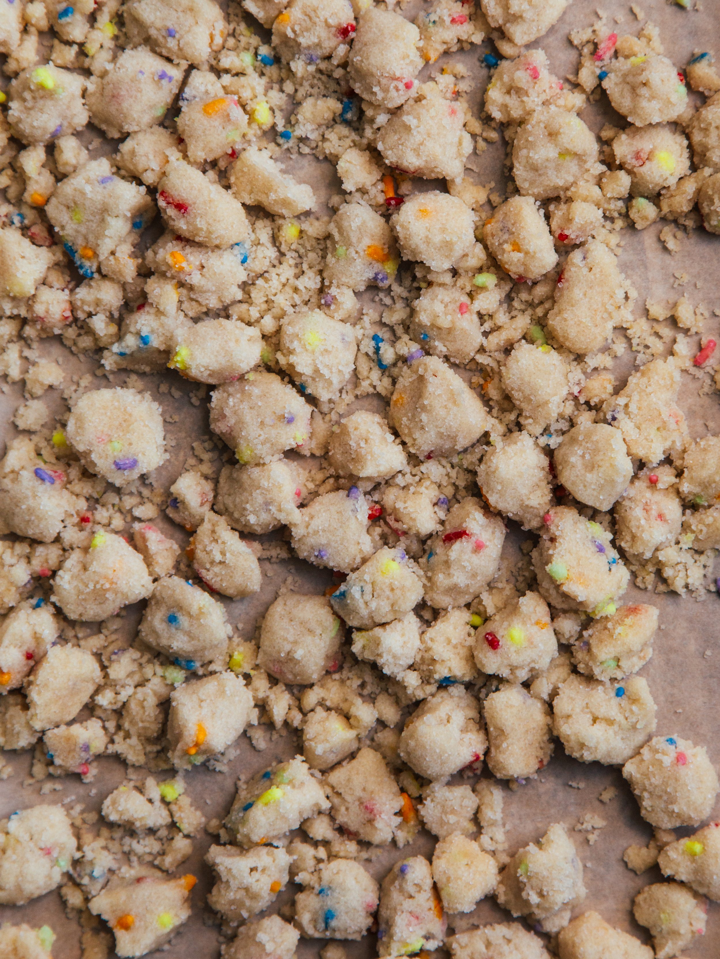 Uncooked cookie dough with colorful sprinkles, spread on parchment paper.