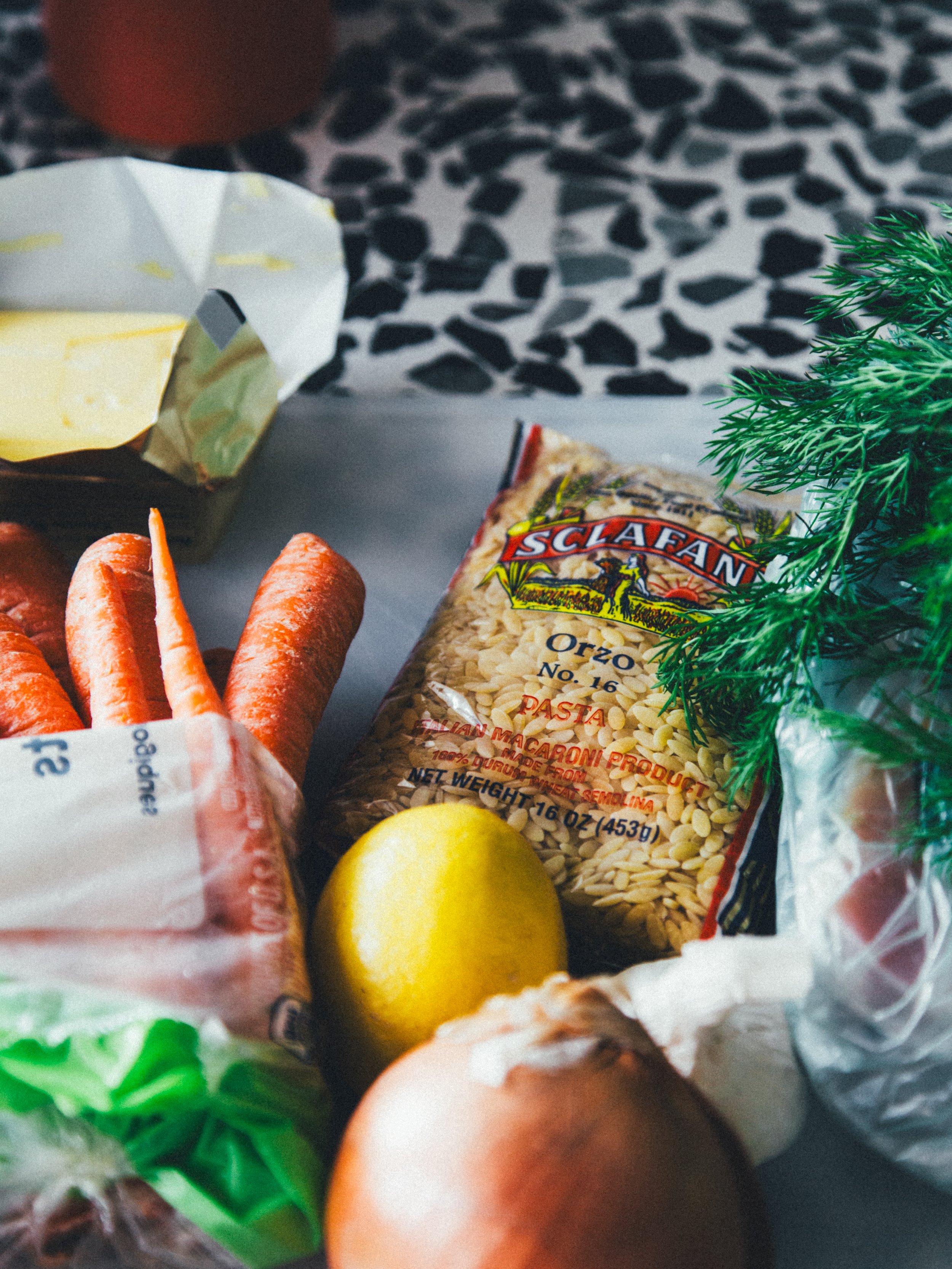 Fresh vegetables including carrots, lemon, onion, and a package of pasta on a countertop.