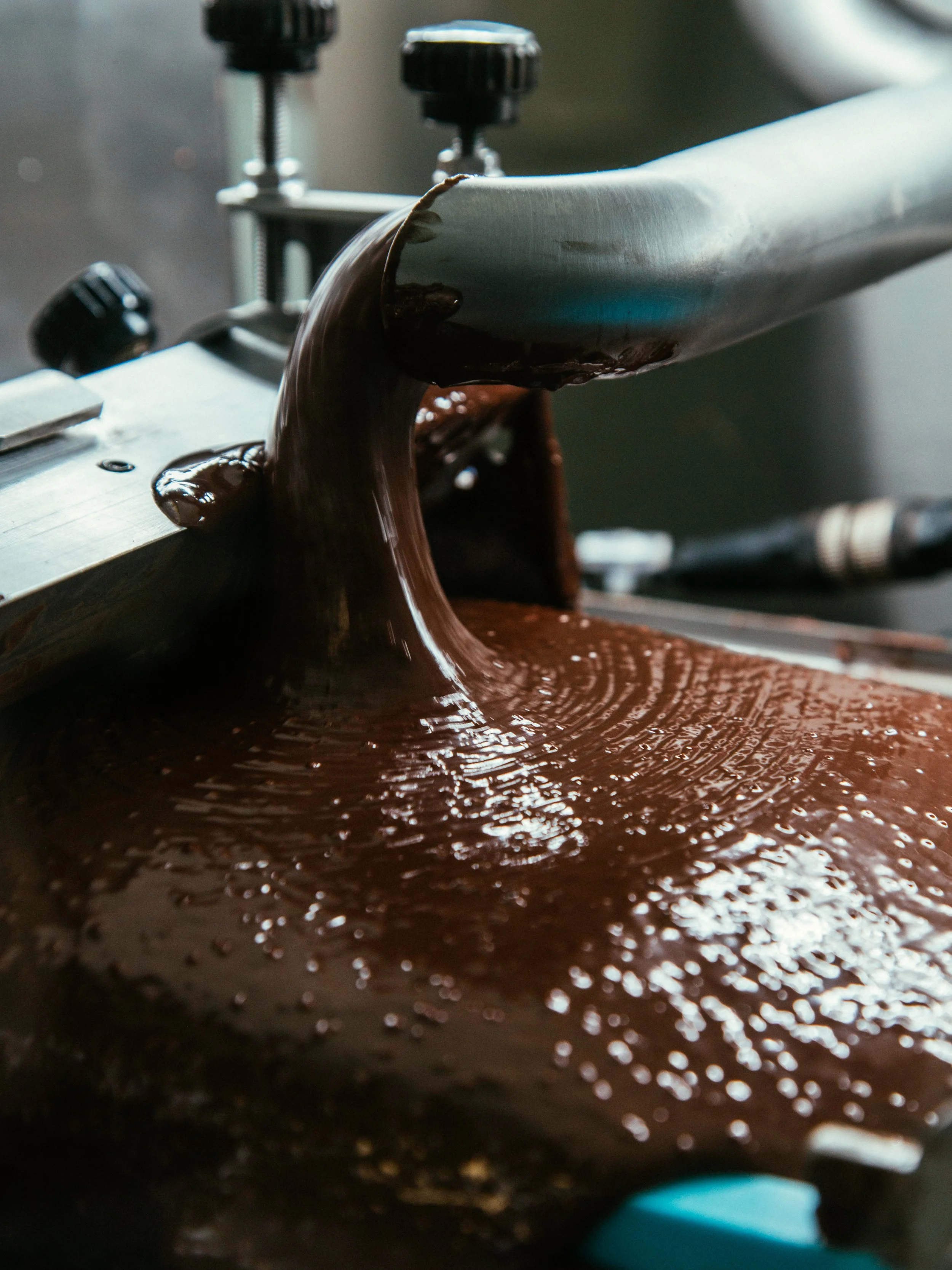 Close-up of melted chocolate being poured on a conveyor belt in a chocolate factory.