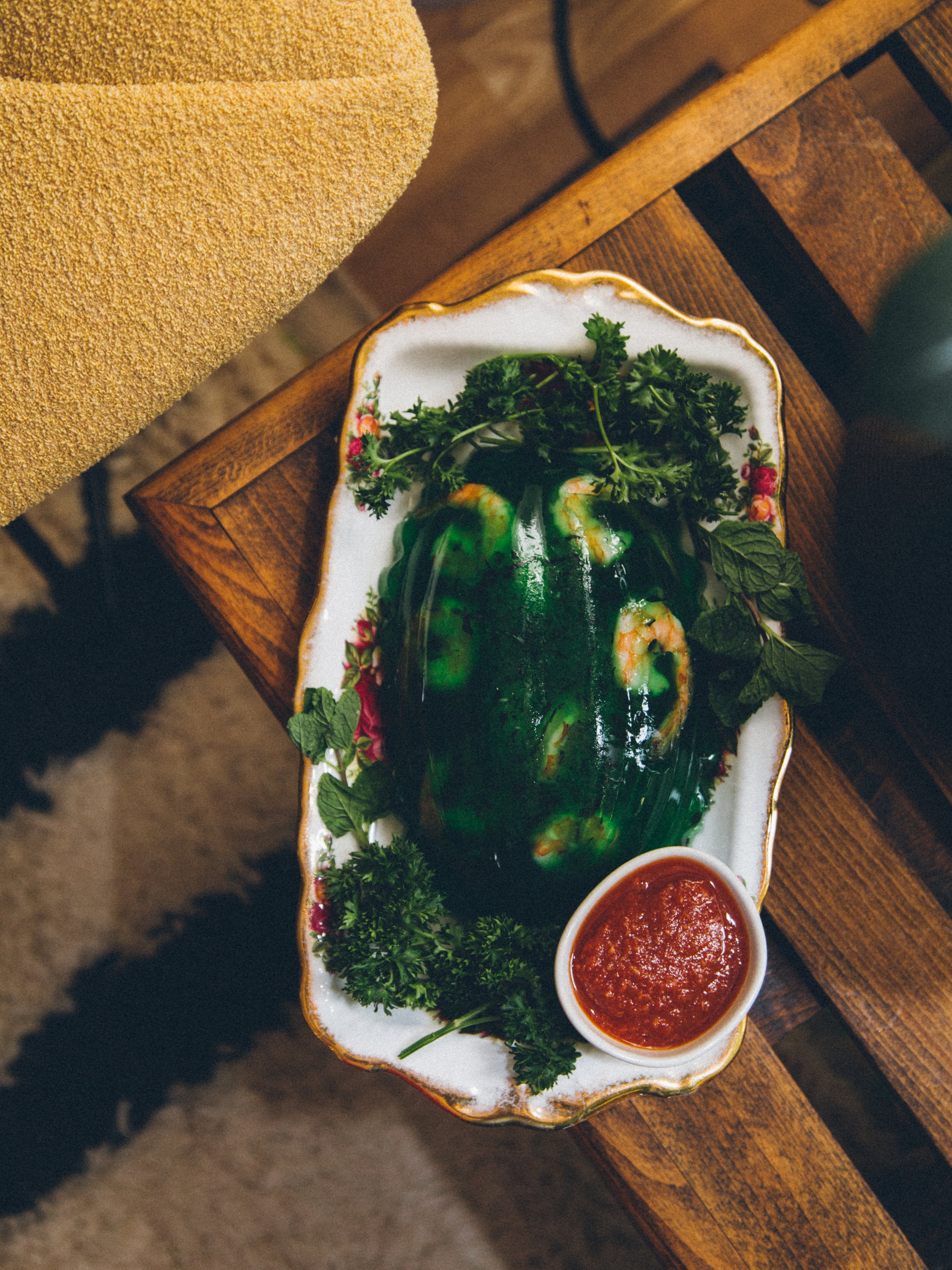 A decorative porcelain platter with a jalapeño pepper, garnished with parsley and mint, served with a side of red sauce on a wooden table.