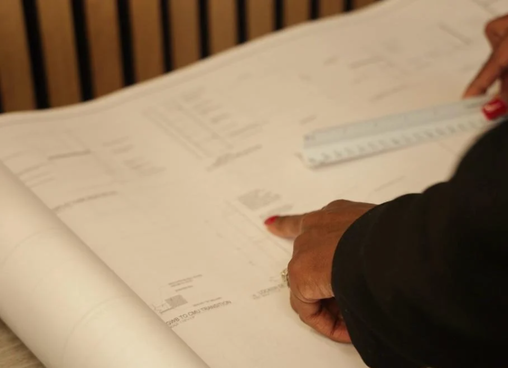 Close-up of a person with red nail polish measuring or pointing at a blueprint or architectural plan on a table.