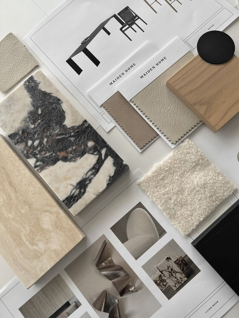 Samples of interior design materials including fabric swatches, marble, wood, and color palette cards on a table with design magazines.