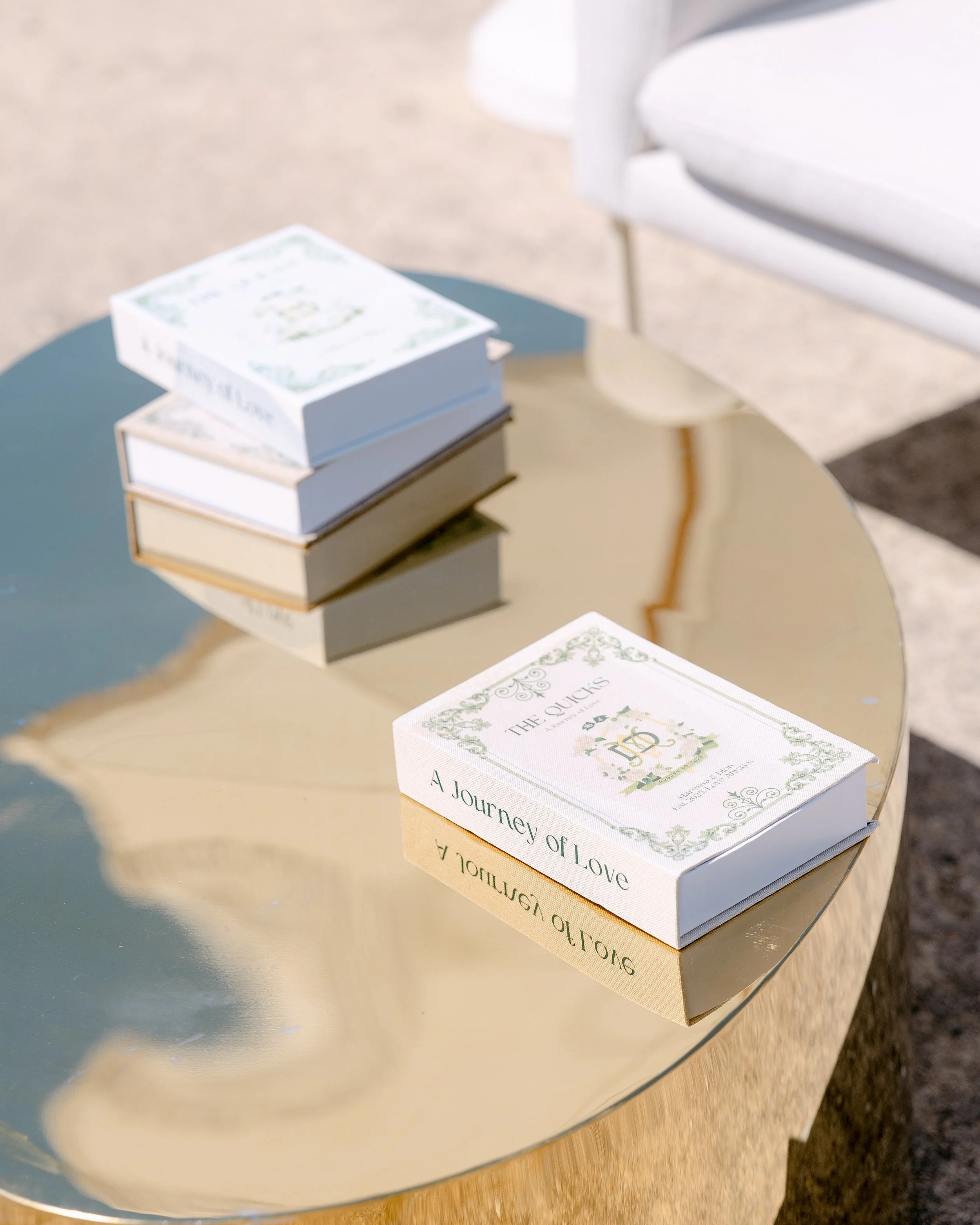 Books titled 'A Journey of Love' and 'The Quicks' on a reflective gold table near a white chair, outdoors.