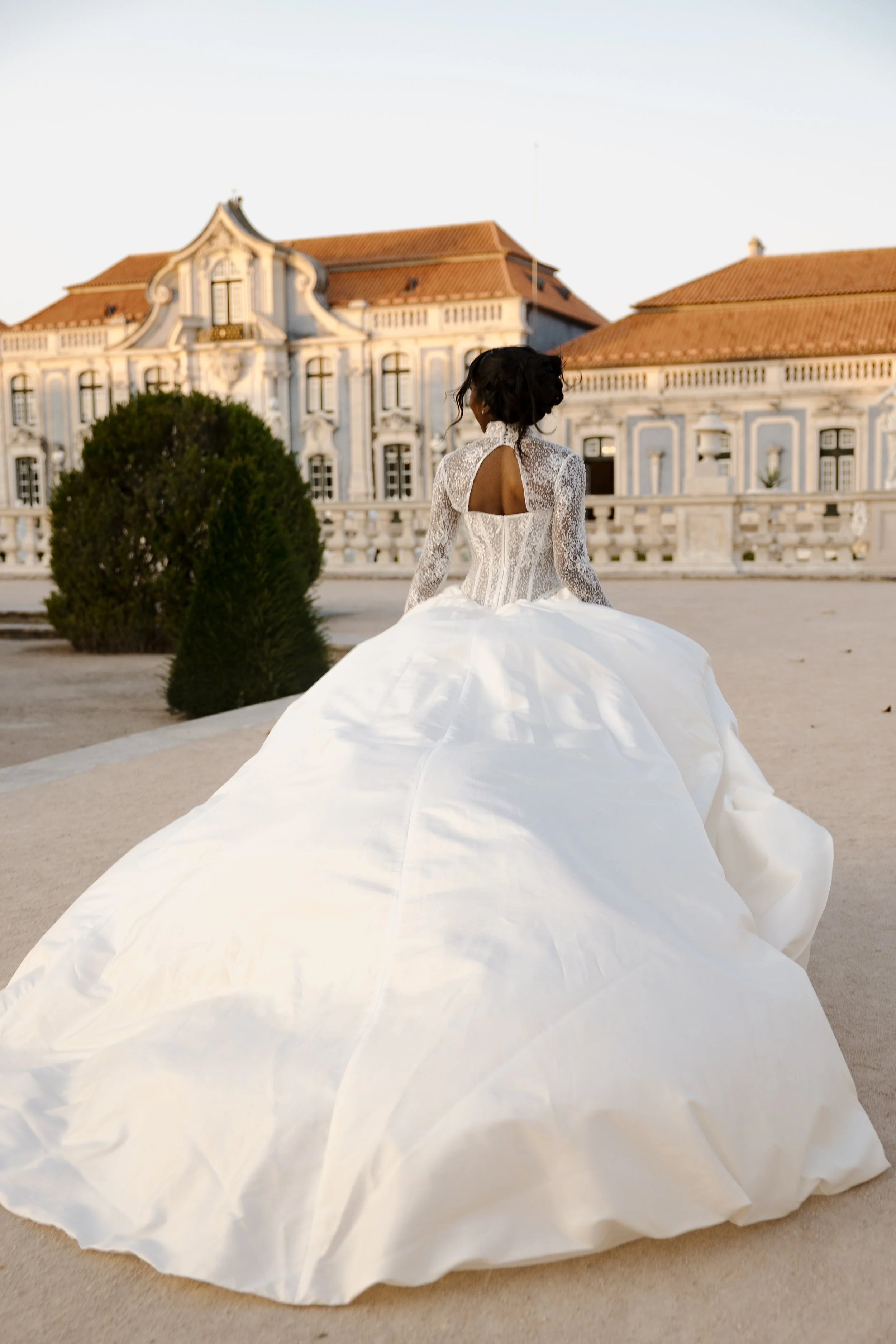 Woman in a white wedding dress standing outdoors in front of a grand, historic building with red-tiled roof.