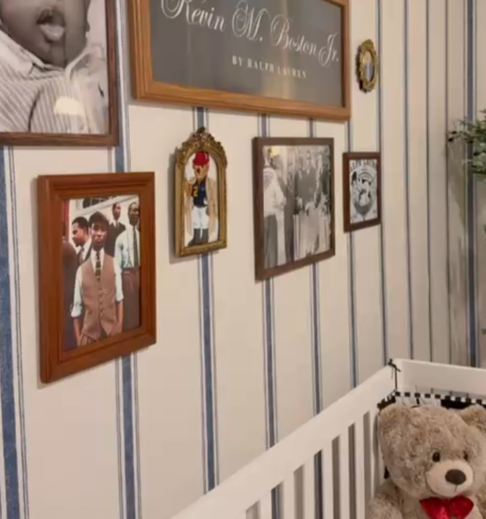 Wall decorated with framed photographs and a chalkboard sign, with a teddy bear in a crib in the foreground.