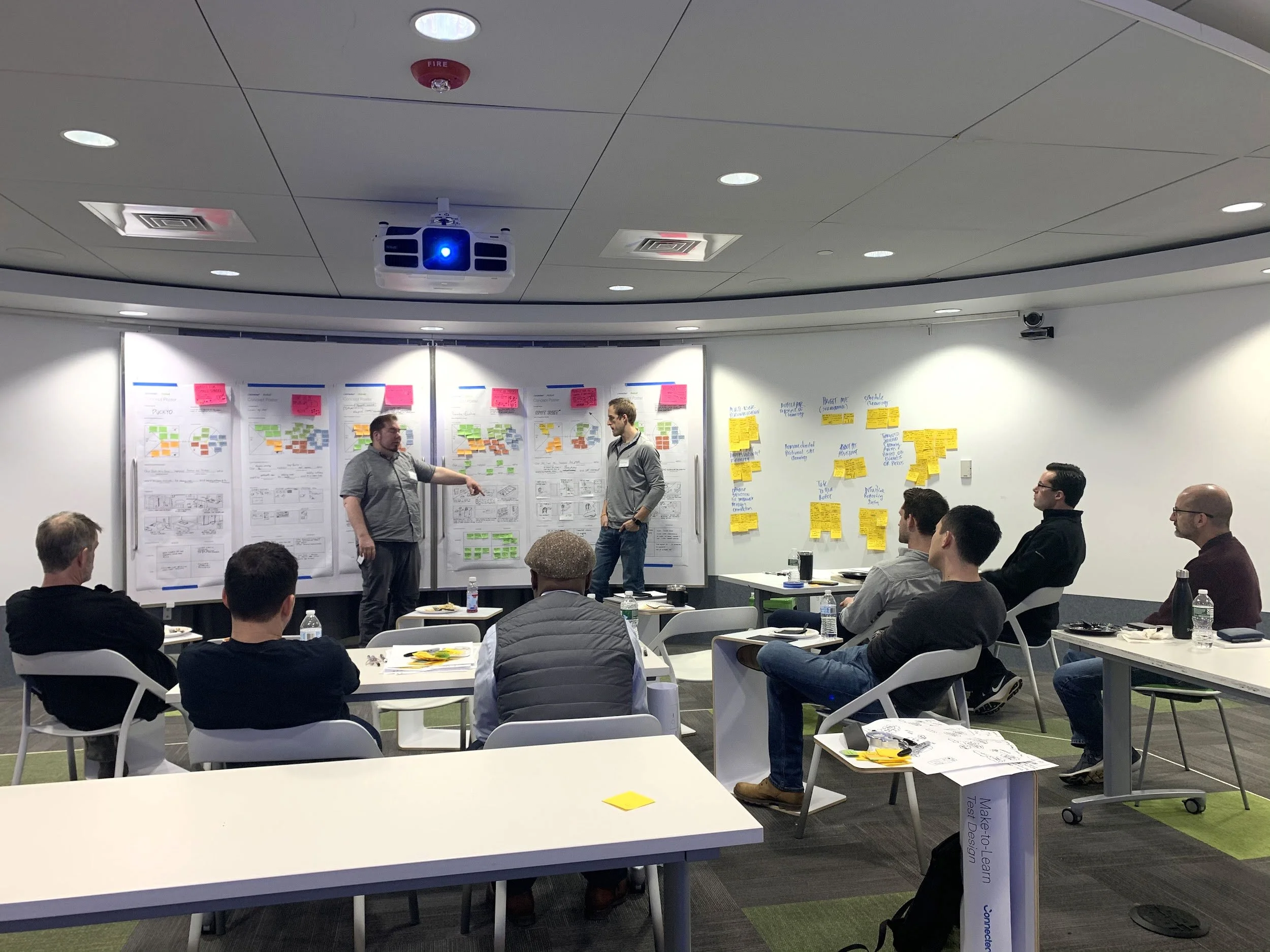 A workshop room with participants seated and two presenters discussing ideas at the front