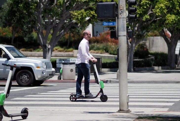 A man riding an electric scooter at a crosswalk near traffic and a traffic light