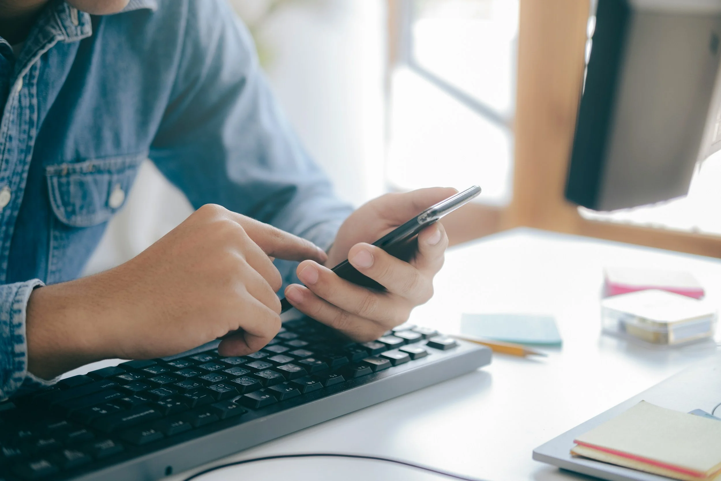 A person using a smartphone while sitting at a desk with a keyboard