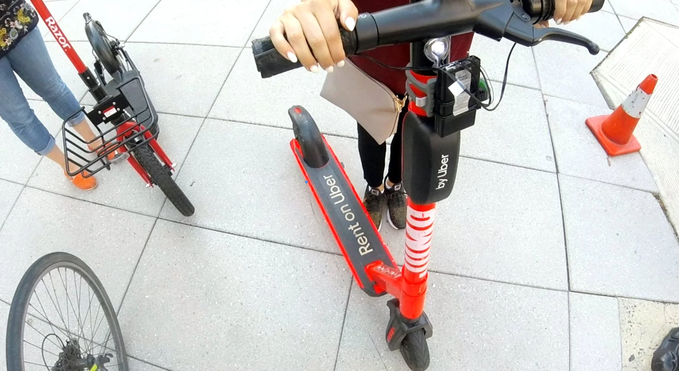 Close-up of a red Uber rental scooter being held by a person with visible hands and a handbag