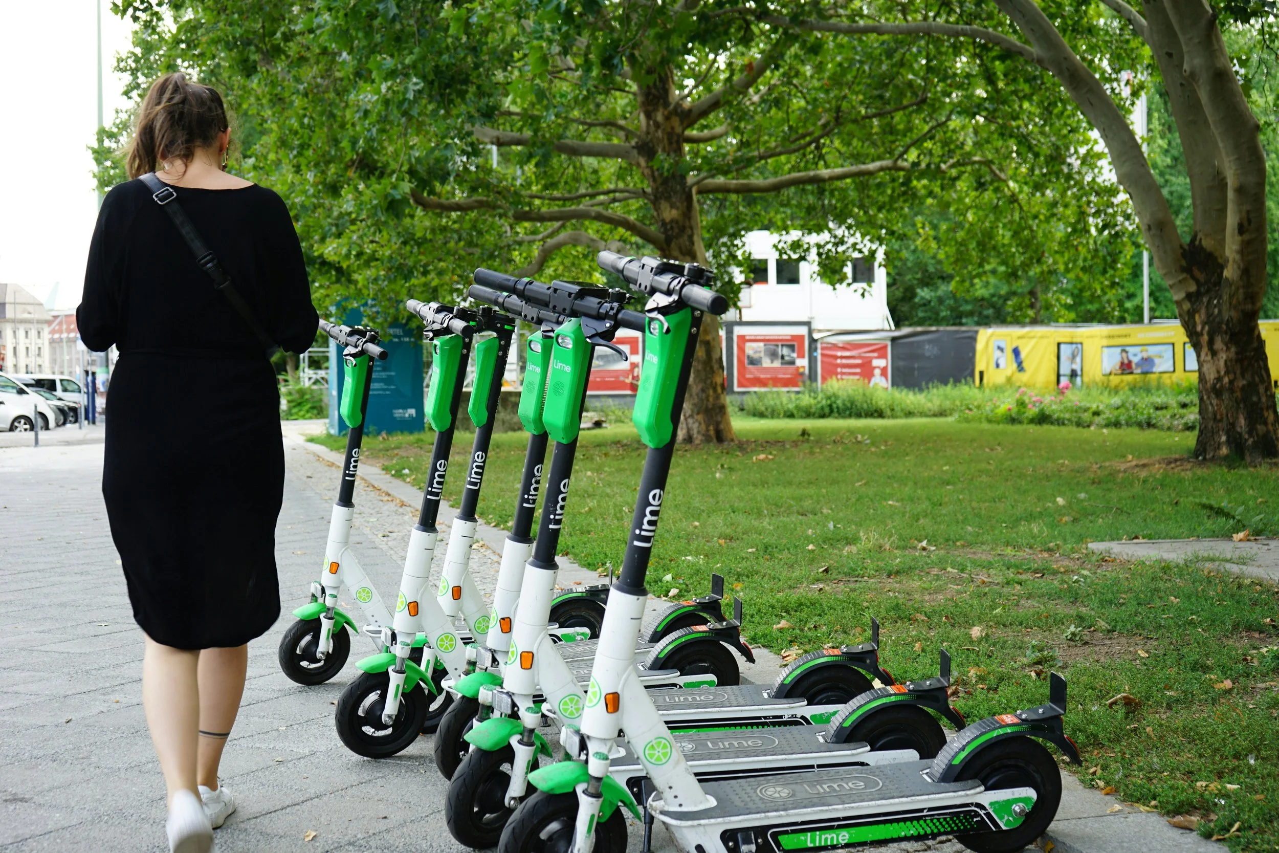 A row of green and white Lime rental scooters parked next to a sidewalk as a woman walks past them