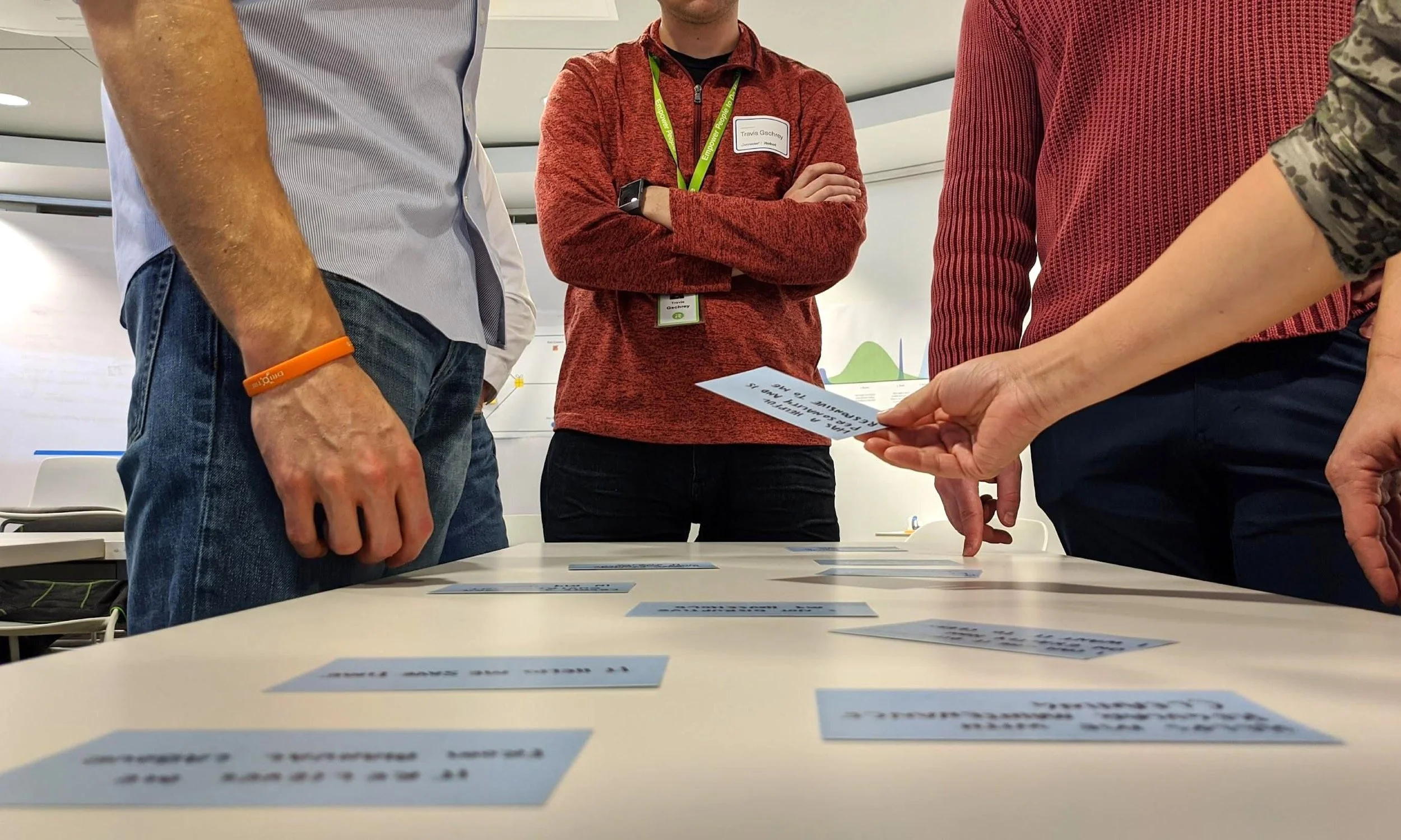 Several people’s hands sorting through labeled paper cards on a table, indicating a collaborative ideation or planning activity