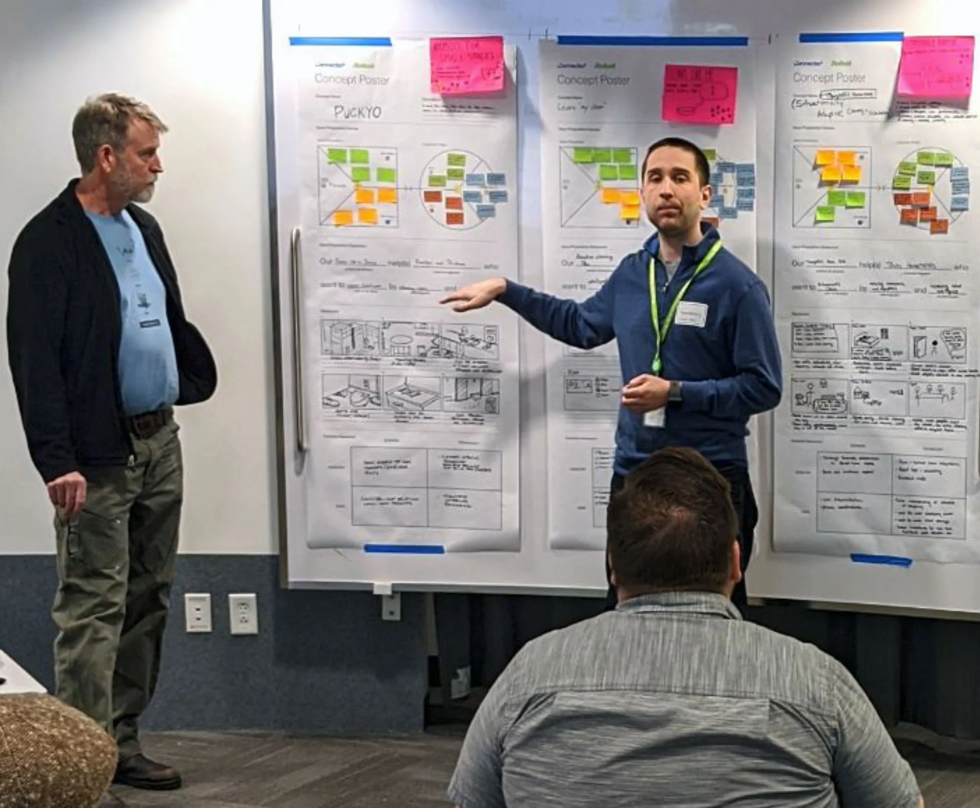 A presenter pointing at a poster with sticky notes and diagrams