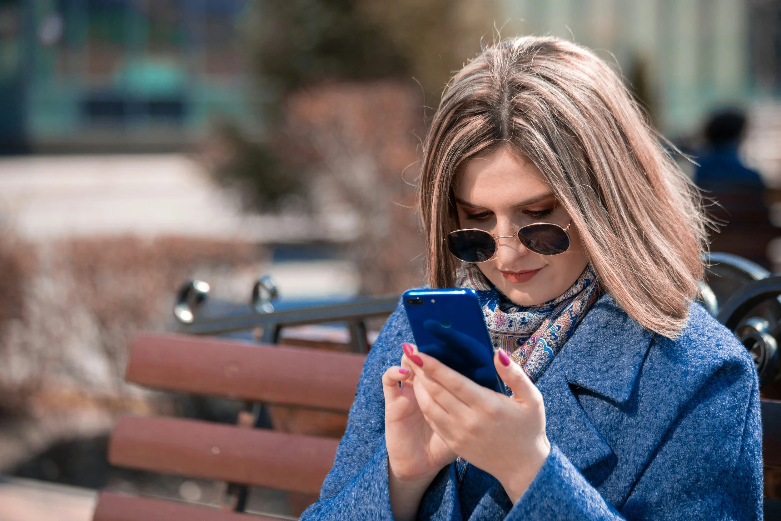 A woman sitting on a bench outdoors, looking at her smartphone outdoors