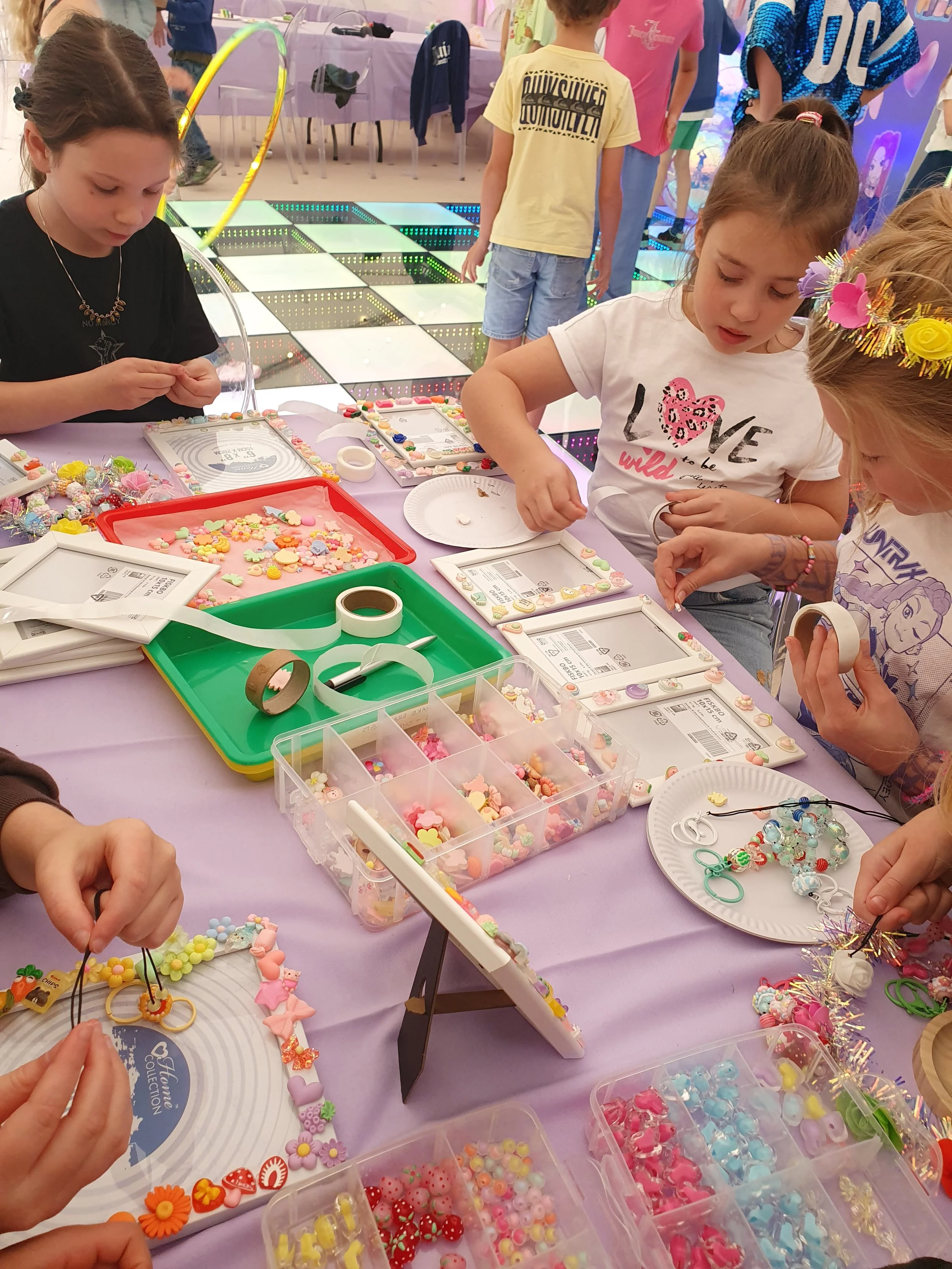 Children making jewelry at a craft table with beads, tape, and jewelry-making tools.