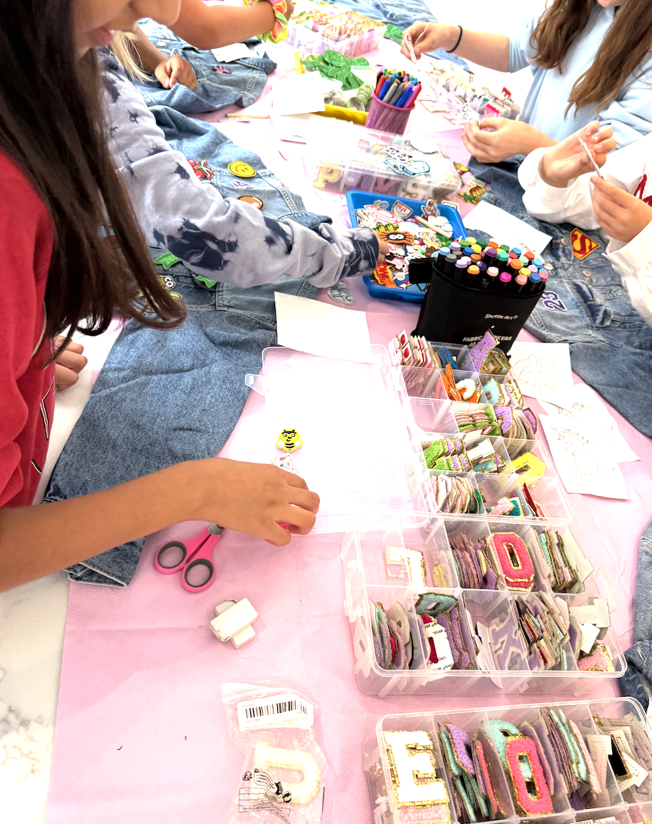 Children making decorated cookies or crafts at a table with colorful supplies, including glittery foam shapes and markers.