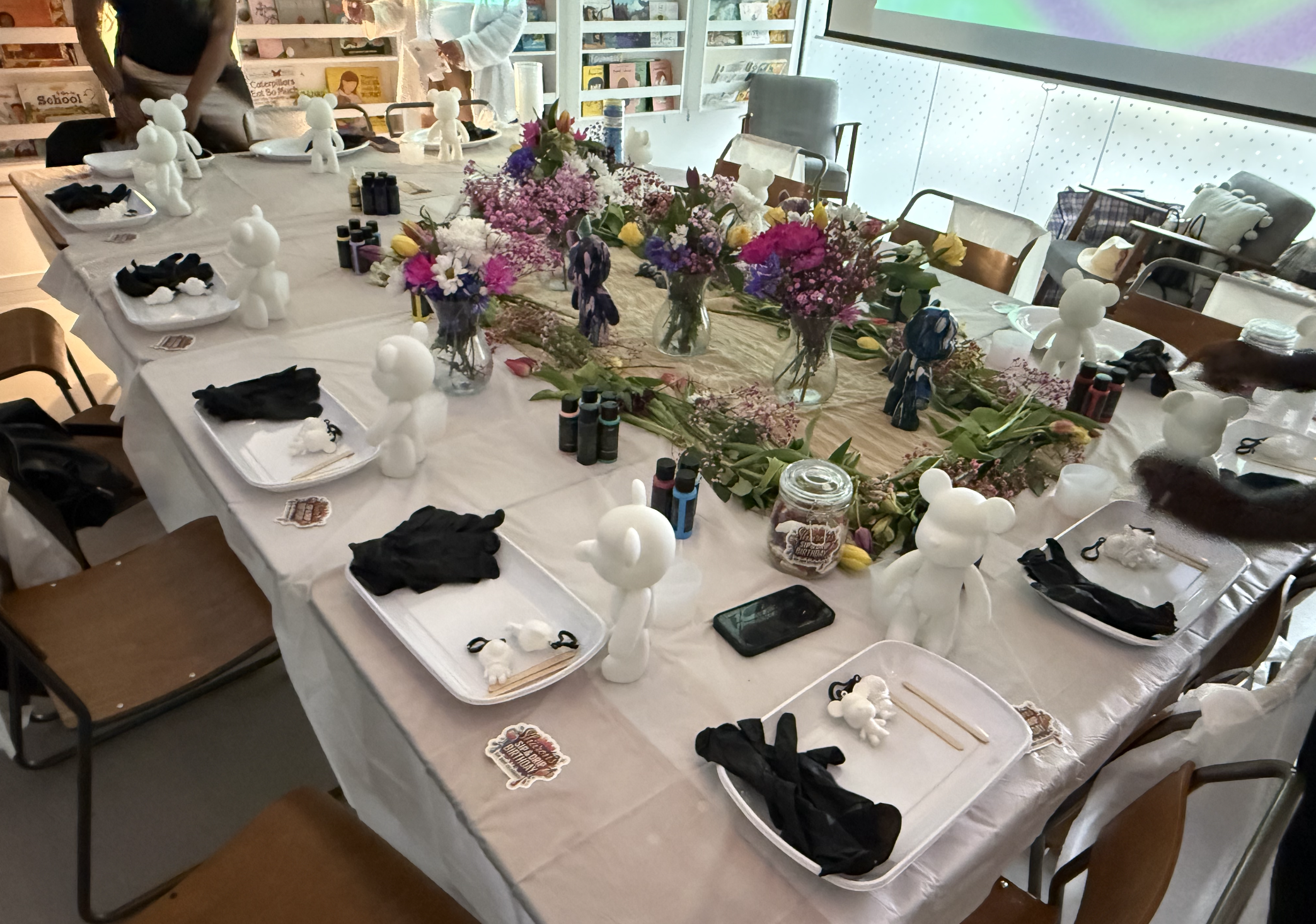 Decorated table with white teddy bear figurines, black gloves, colorful flower centerpieces, and empty plates and utensils, ready for an event.