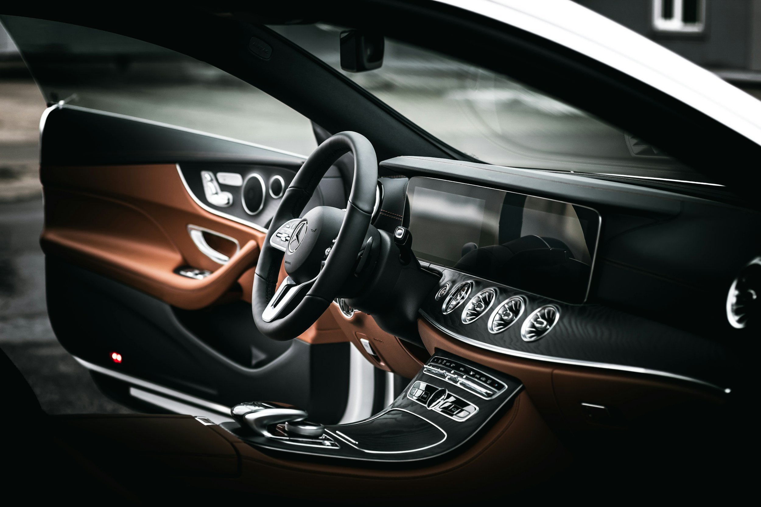 Luxury car interior with black steering wheel, digital dashboard, brown leather accents, and center console with silver controls.
