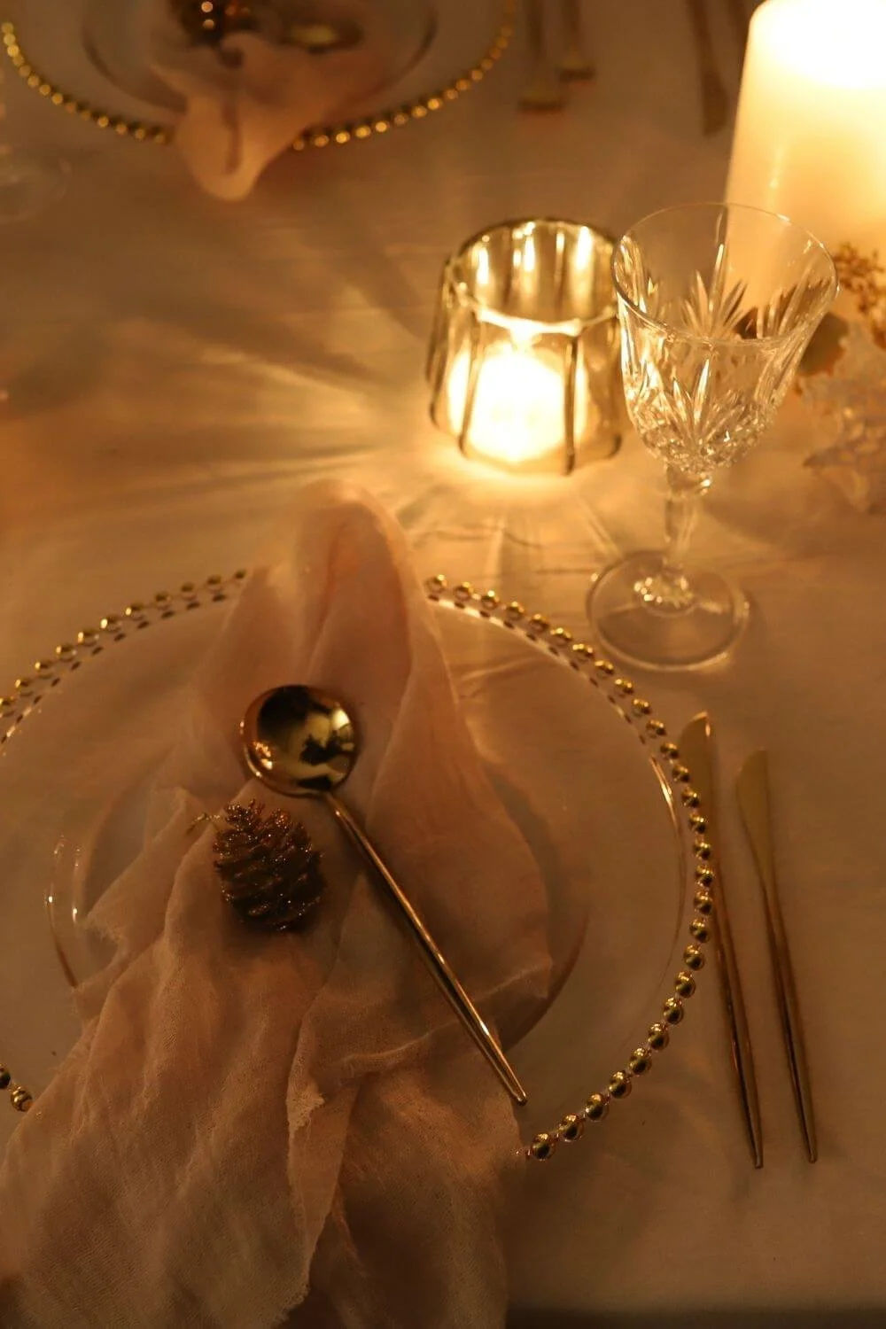 Nahaufnahme einer modernen Tischdeko zu Weihnachten mit goldfarbenem Besteck, Stoffservietten und sanftem Kerzenlicht – stilvolle Tischdetails.