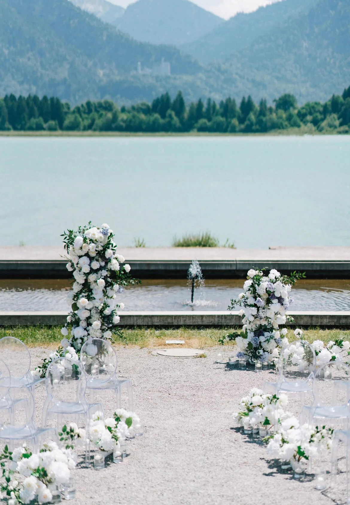 Freie Trauung bei einer Gartenhochzeit am See mit Blumenarrangement und Stuhlreihen mit Ghost Chairs von de Waay im Grünen