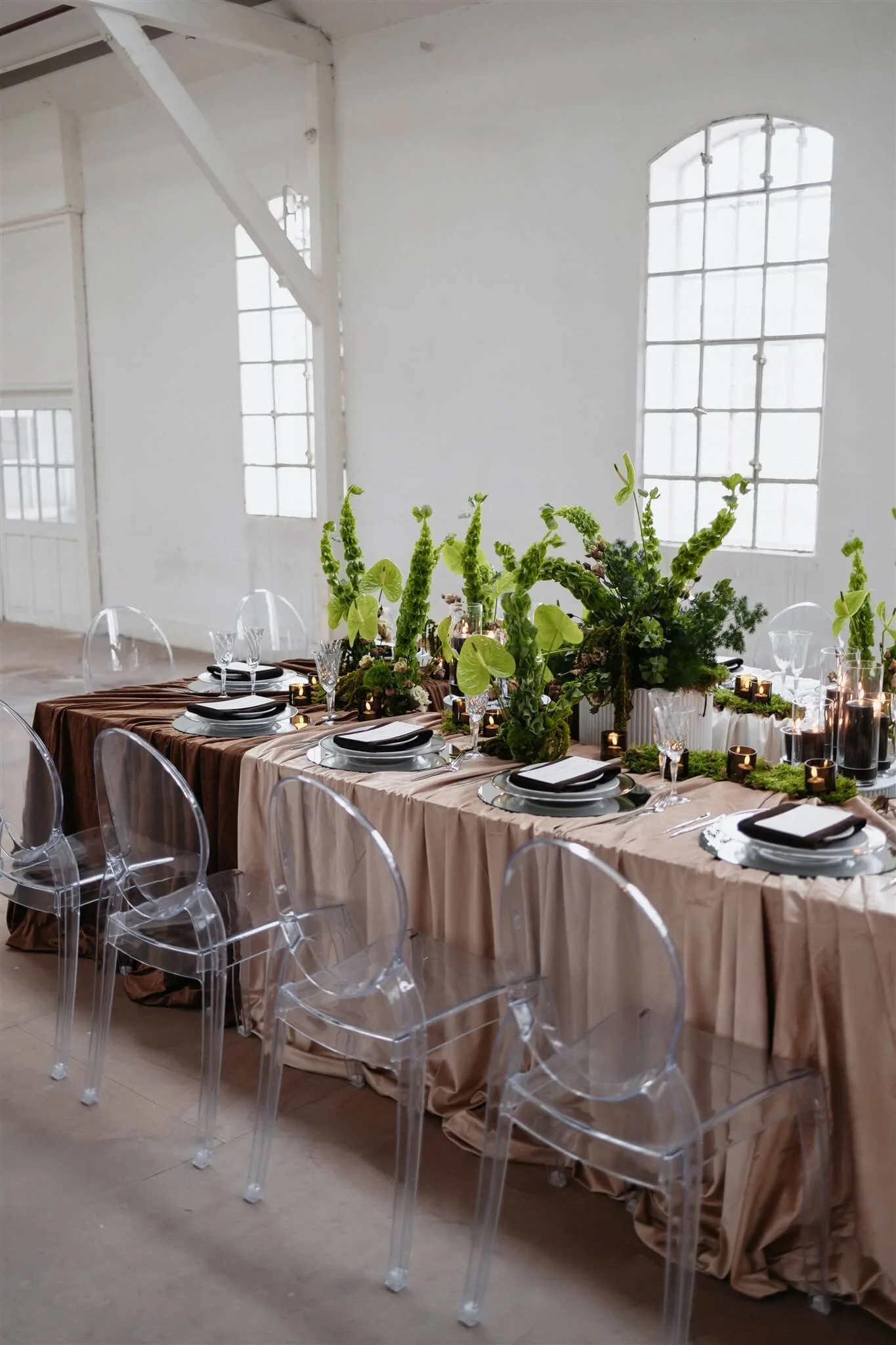 Hochzeitsfarben 2026: Hochzeitstafel mit Tischdecken in warmen Neutrals, Brauntönen, grüner Floristik und transparenten Ghost Chairs von de Waay