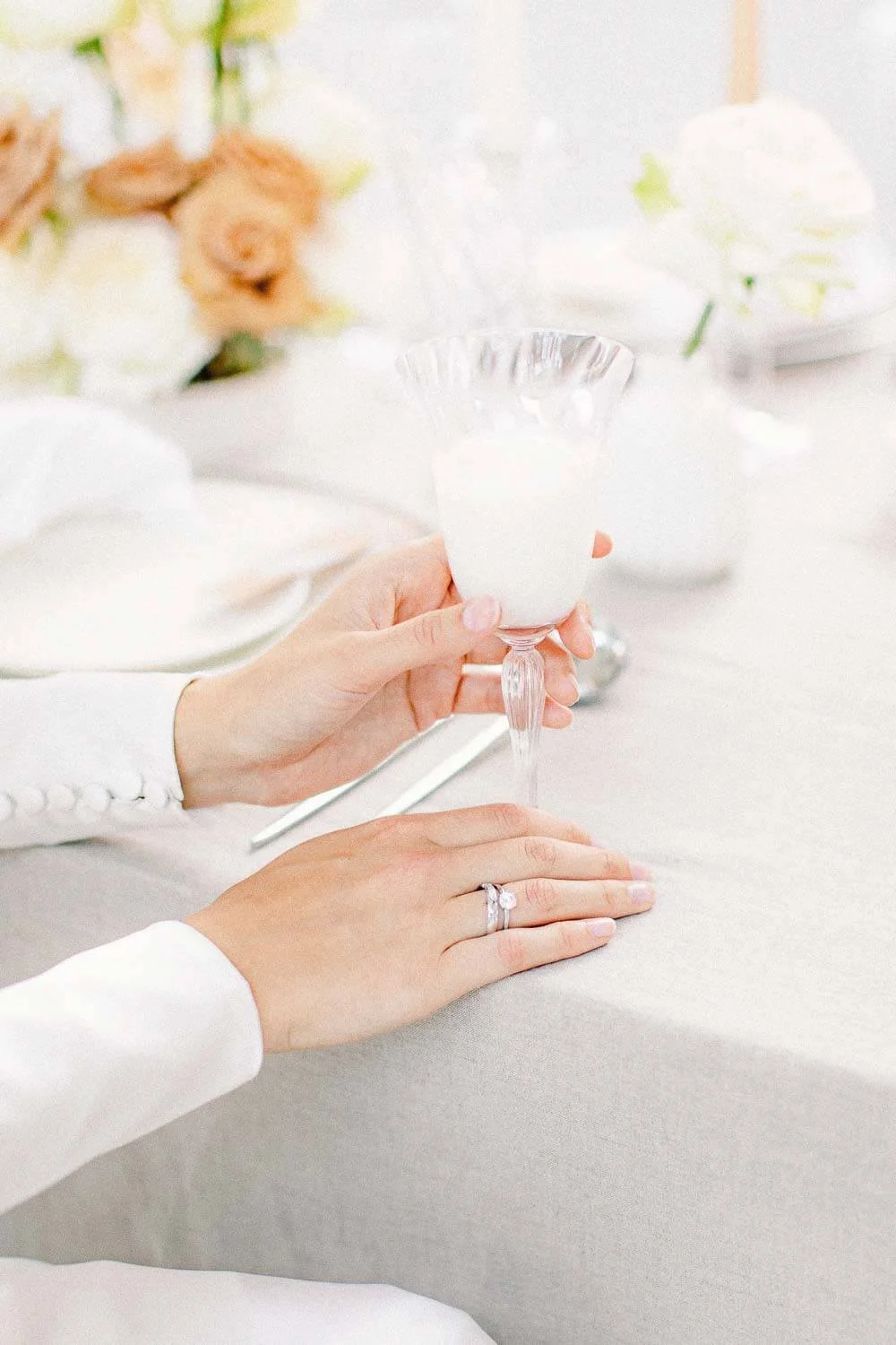 Guest holding a glass at a softly styled wedding table with minimal decor and warm candlelight