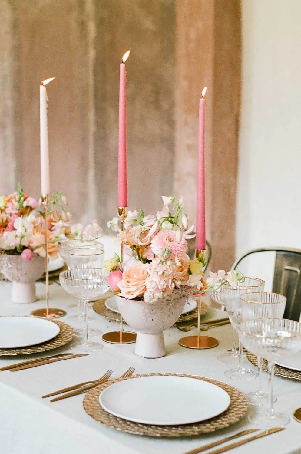 Detailaufnahme einer Hochzeitstafel mit rosegoldenen Platztellern, Kupferbesteck, pinken Stabkerzen und Floristik in Apricot- und Coral-Tönen von de Waay