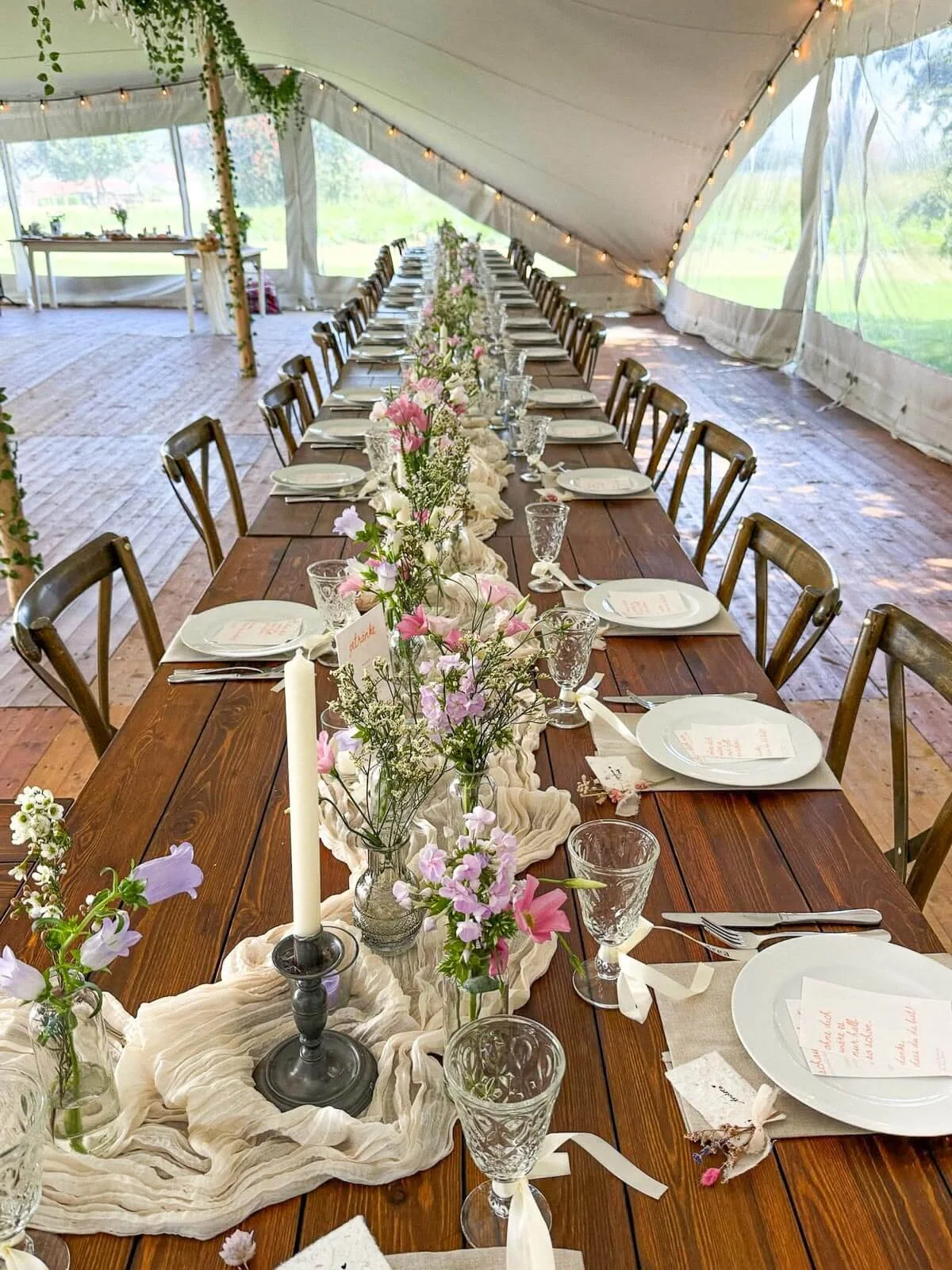 Zelthochzeit mit Lichterketten, langen Holztischen, lockeren Textilien und natürlicher Tischdeko – warme Atmosphäre im Hochzeitszelt