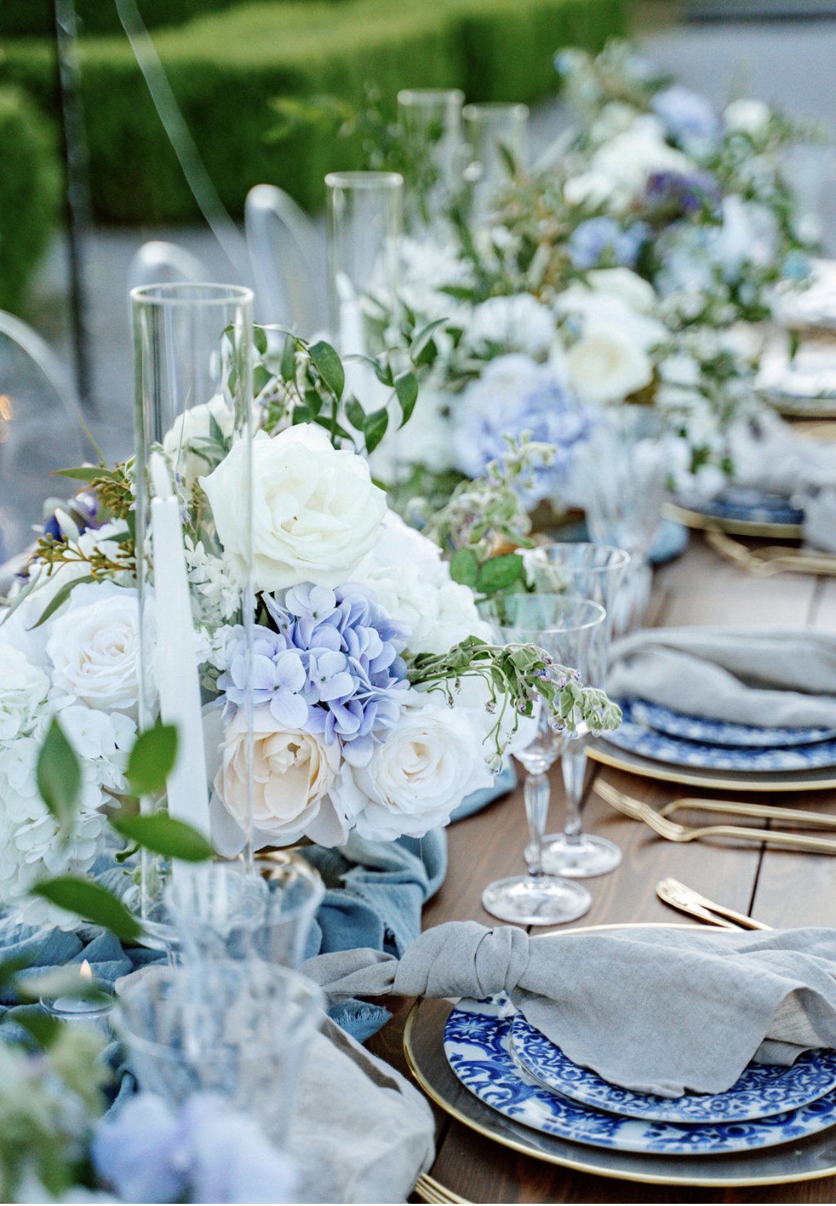 Blaue Tischdeko zur Hochzeit: Blau-weiße Hochzeitsblumen und elegante Gläser auf rustikalem Holztisch mit goldenem Besteck von de Waay