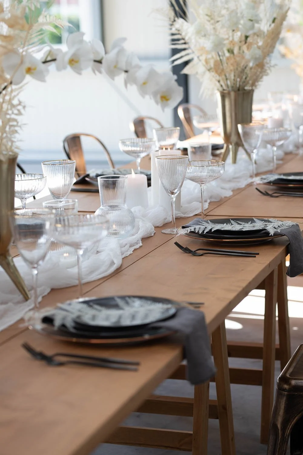 Simple wedding table decorations for long tables with wooden banquet table, black plates, linen runner, glassware, candles and repeated minimalist styling