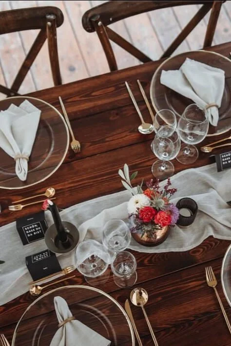 Edited rustic wedding table decor with wood table, linen runner, candlelight and minimal floral arrangement by de Waay