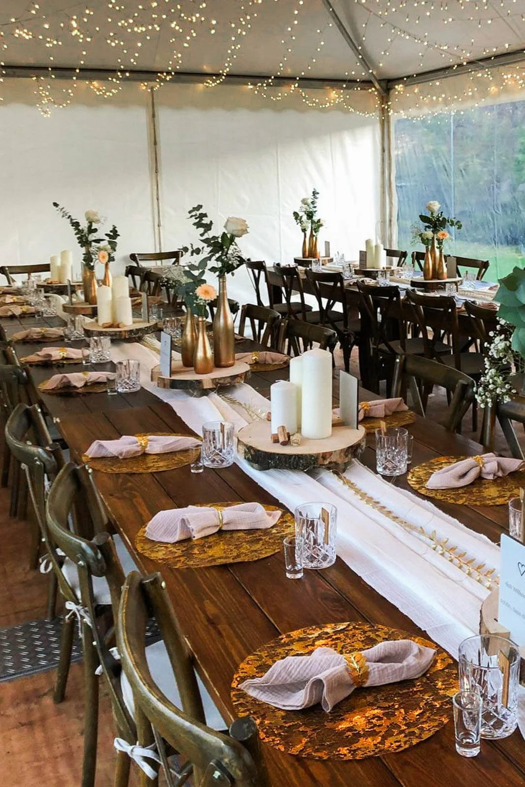 Stimmungsvoll gedeckter Tisch im Zelt mit Lichterketten, Holztischen und warmem Licht – ruhige Atmosphäre bei einer gut geplanten Zelthochzeit