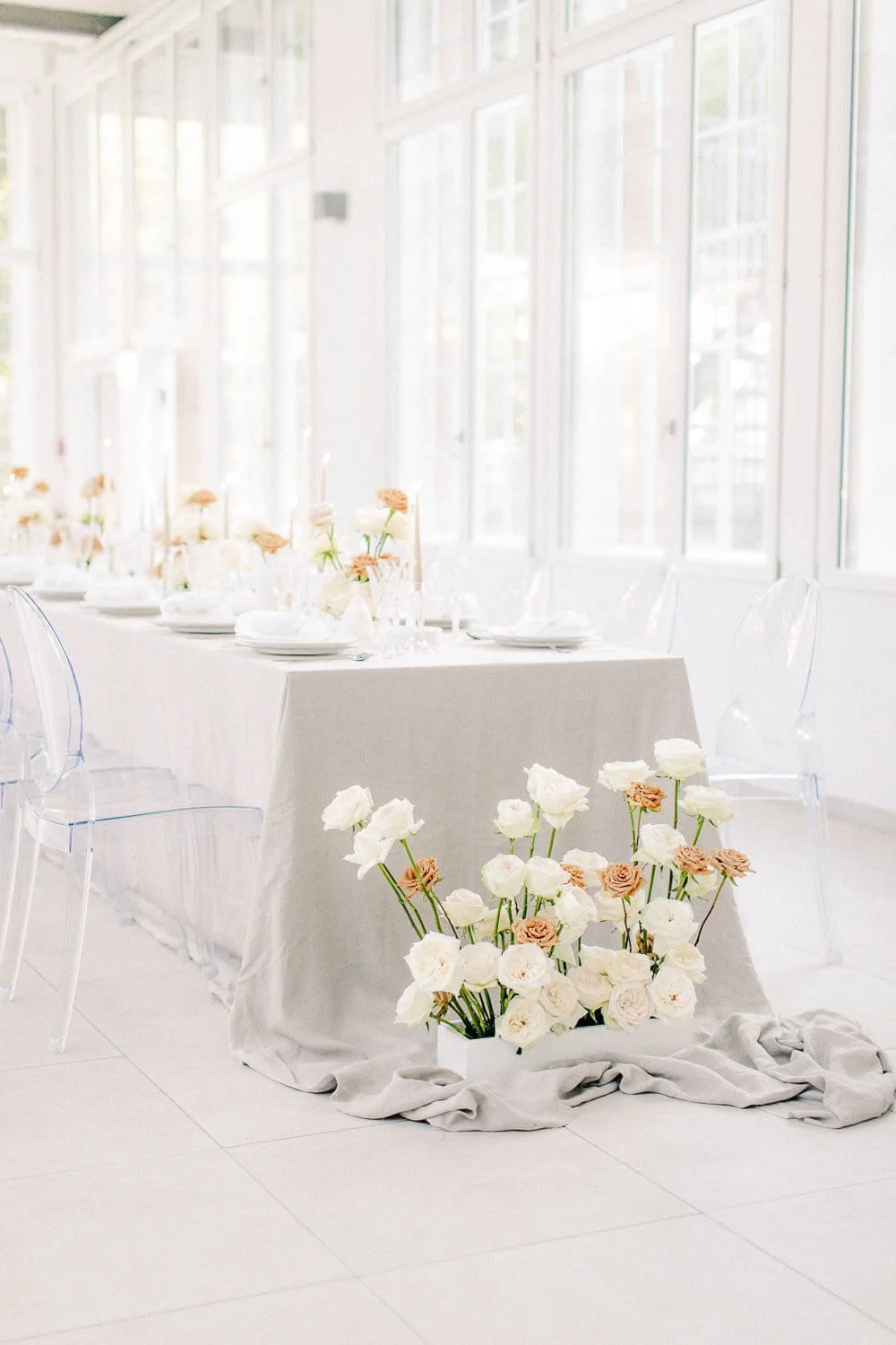 Simple wedding table decorations on a long table with neutral linen tablecloth, taper candles, glassware and soft rose florals by de Waay