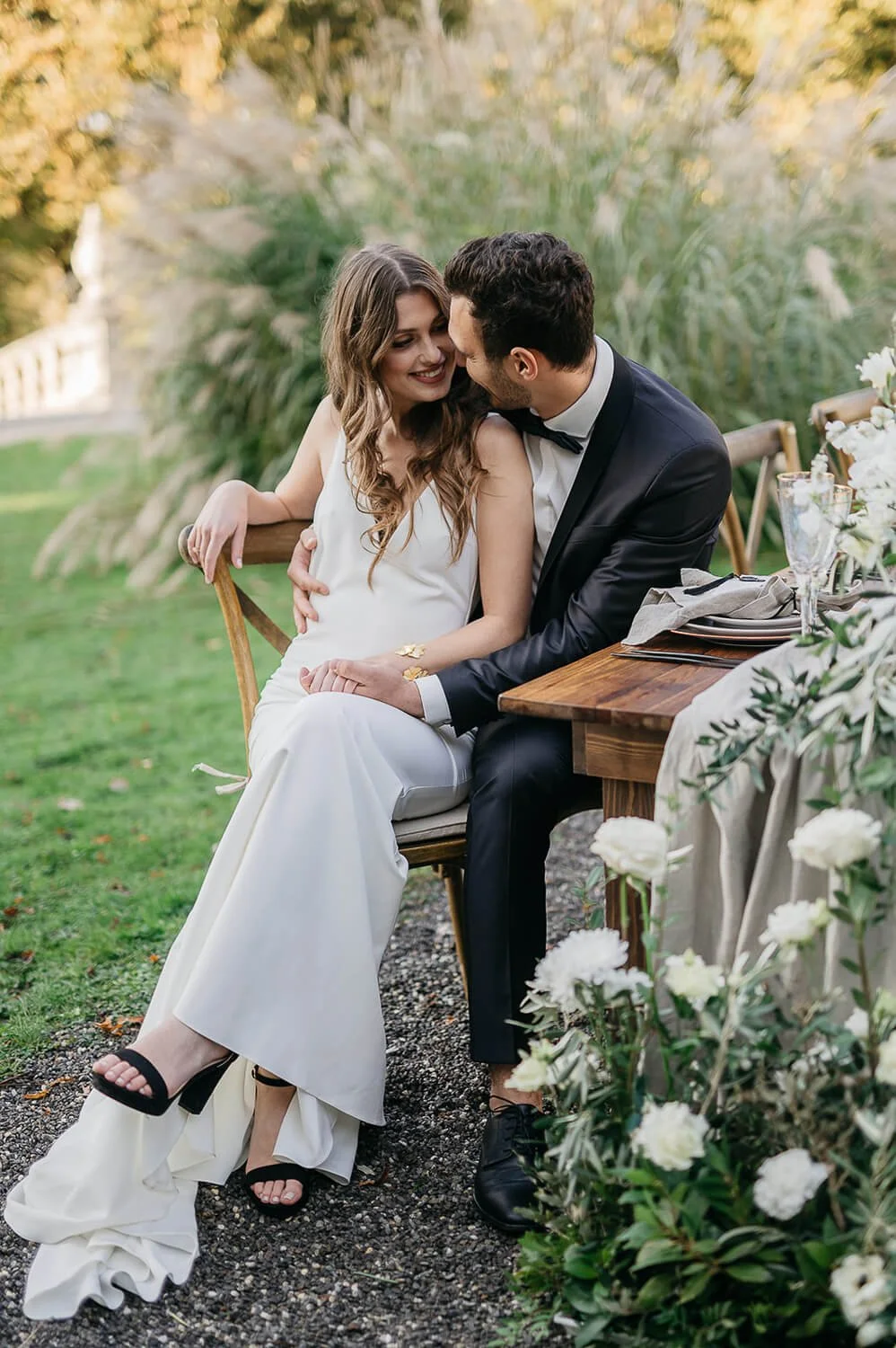 Entspanntes Brautpaar sitzt im Garten an Holztisch von de Waay – Gartenhochzeit für Paare, die Nähe, Ruhe und klare Entscheidungen schätzen