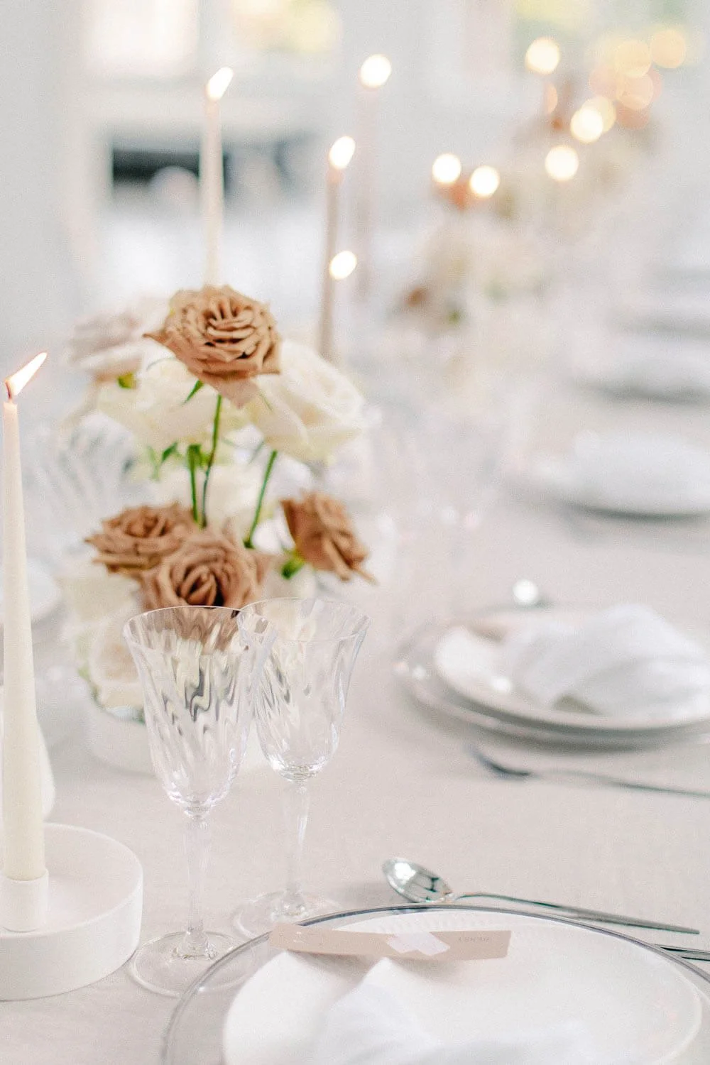 Simple wedding table decoration ideas with candles, crystal glassware, white place setting and neutral rose florals by de Waay