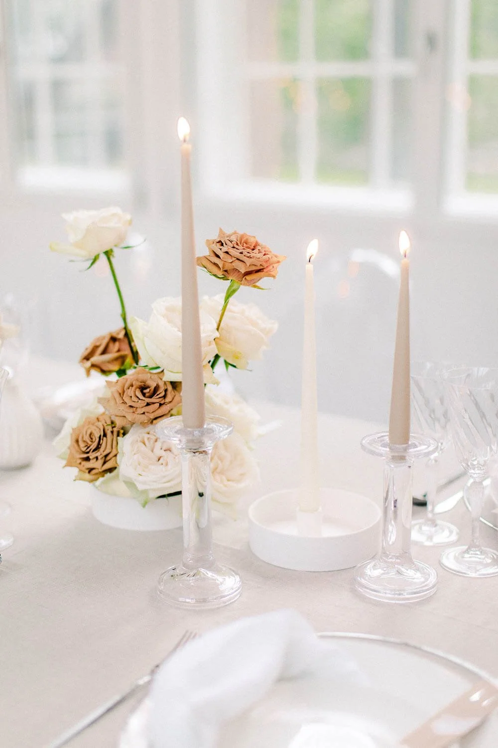 How to decorate a wedding table simply with taper candles, neutral rose centerpiece, clear glassware and white place setting by de Waay