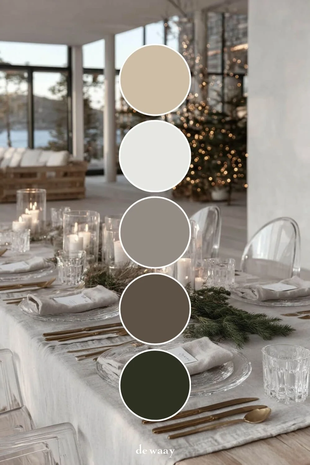 Eleganter Weihnachtstisch mit Tannengrün, großen Kerzenzylindern, Kristallgläsern und Goldbesteck vor einem beleuchteten Baum.