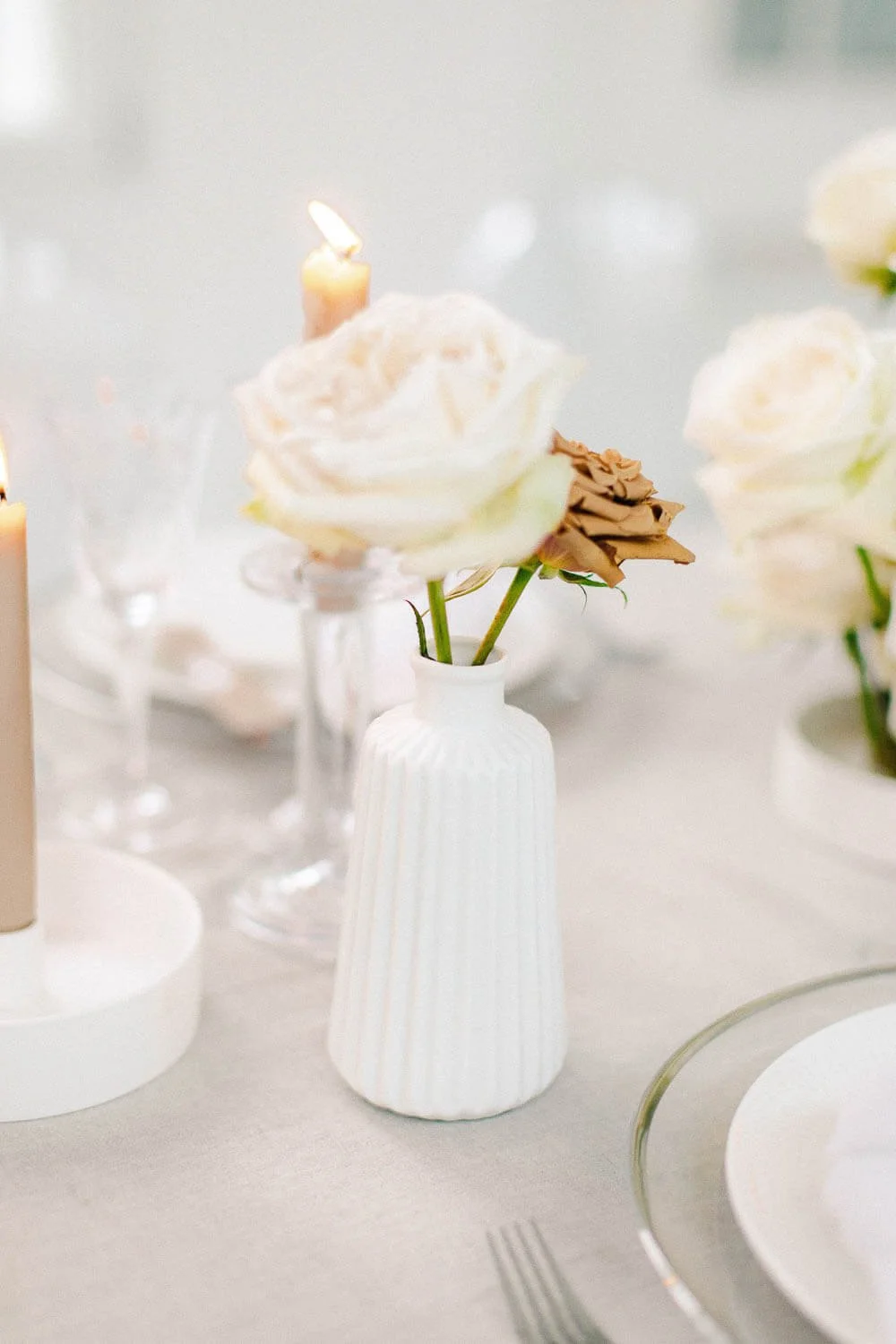 Minimal wedding table with a single bud vase of ivory and taupe roses, soft candlelight and clean neutral styling