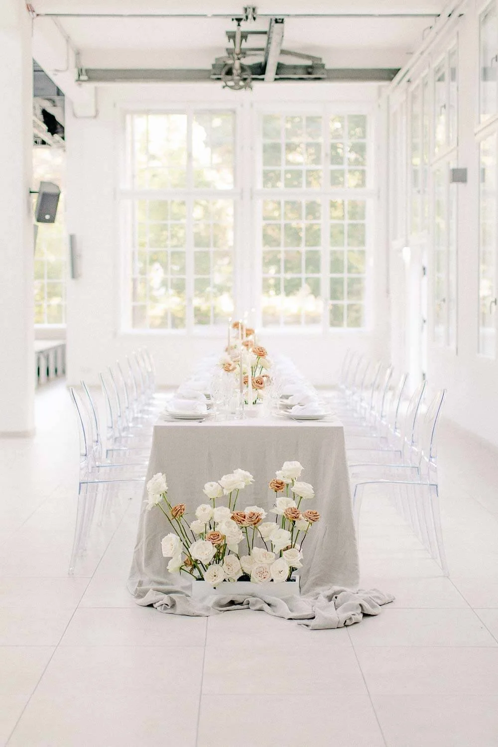 Simple wedding table with neutral linen tablecloth, plates, glassware, candles, floral arrangement and ghost chairs by de Waay