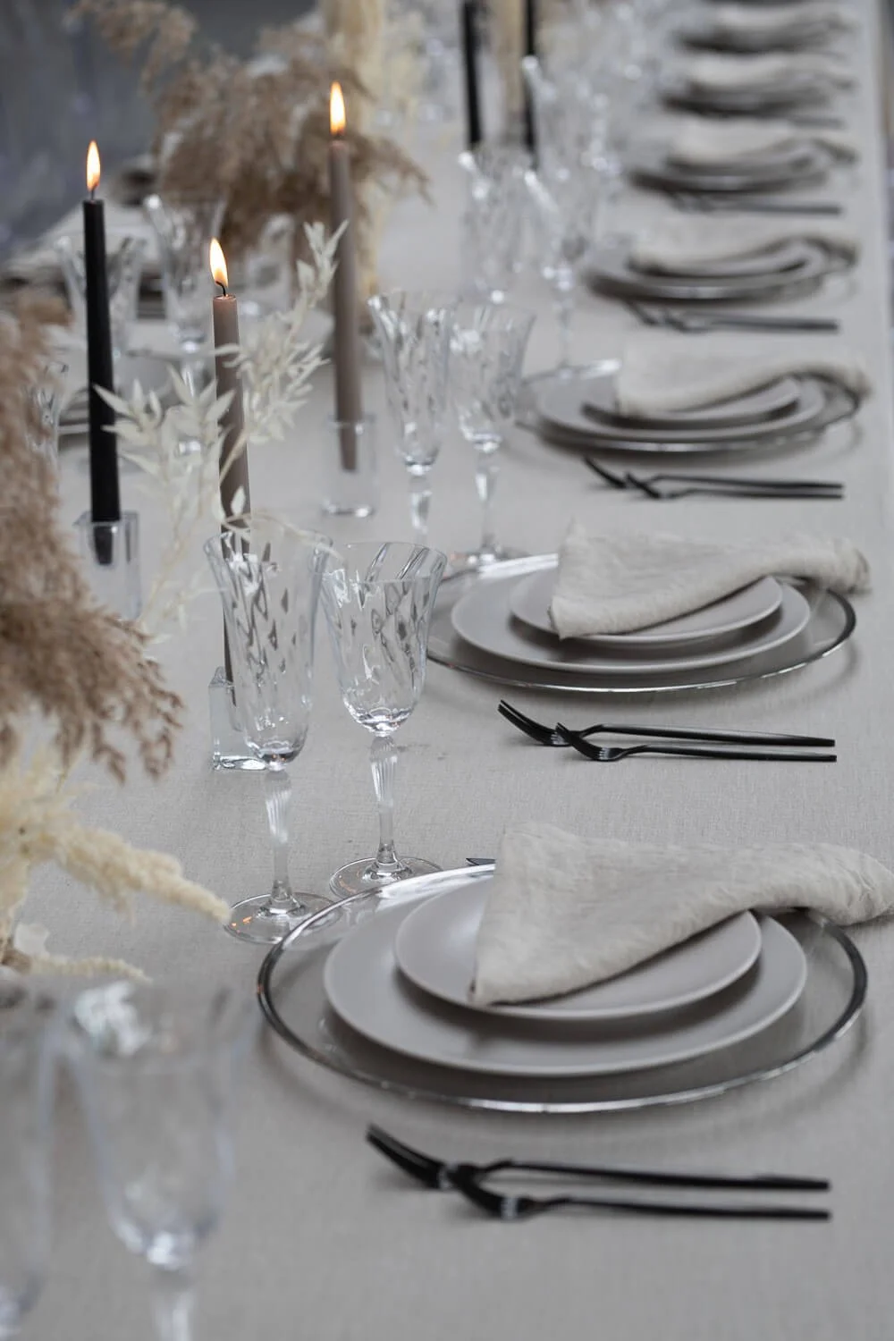 Modern wedding table decor with black cutlery, neutral linen tablecloth, taper candles, clear glassware and minimalist floral styling by de Waay