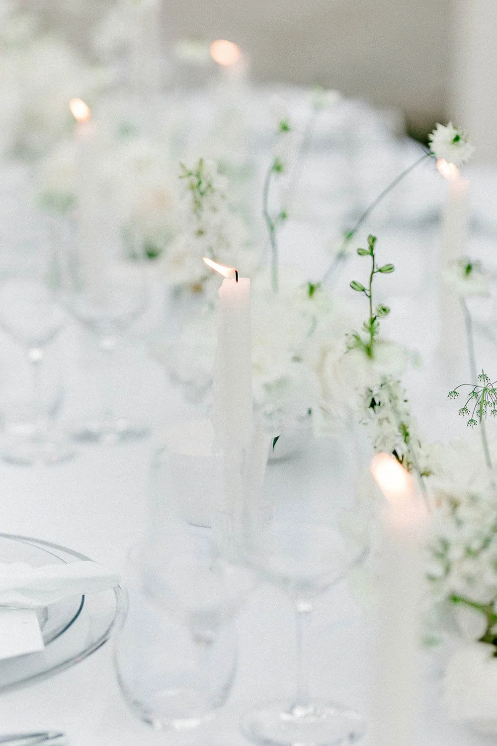 Weiße Tischdeko bei einer Hochzeit mit Kerzen, Glasvasen und feiner weißer Floristik mit Platztellern und silbernem Besteck von de Waay