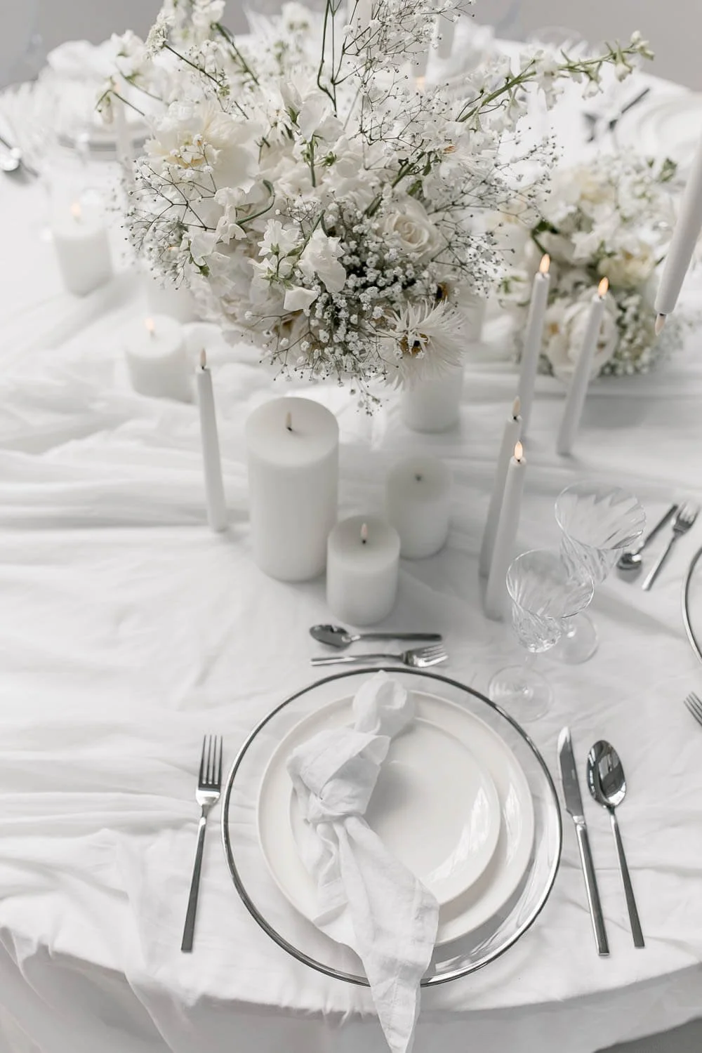 Simple wedding table decorations for round tables with white floral centerpiece, candles, linen tablecloth and balanced minimal styling
