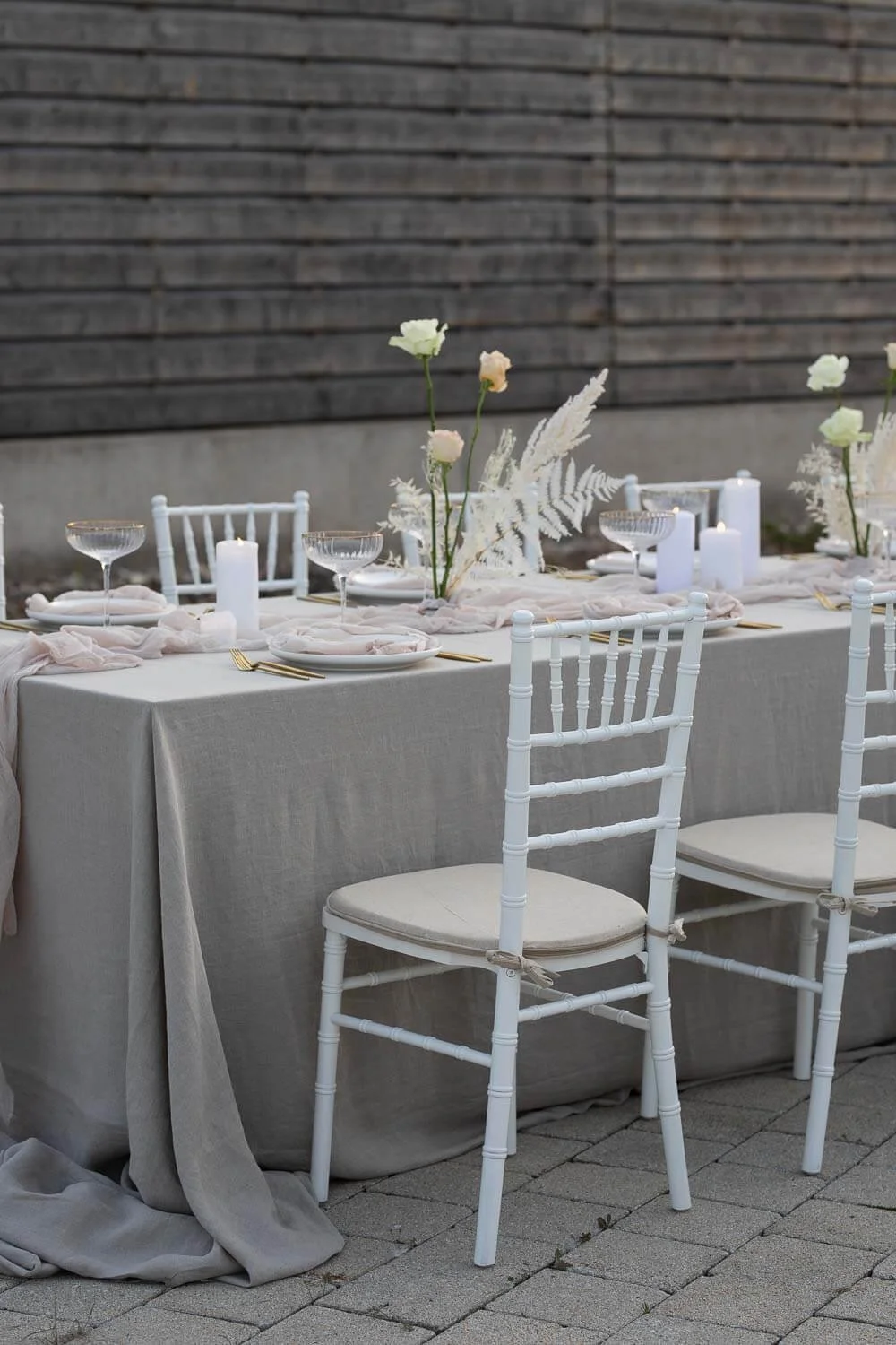 Simple outdoor wedding table decor with neutral linen tablecloth, soft napkins, candles, minimal florals and white tiffany chairs by de Waay