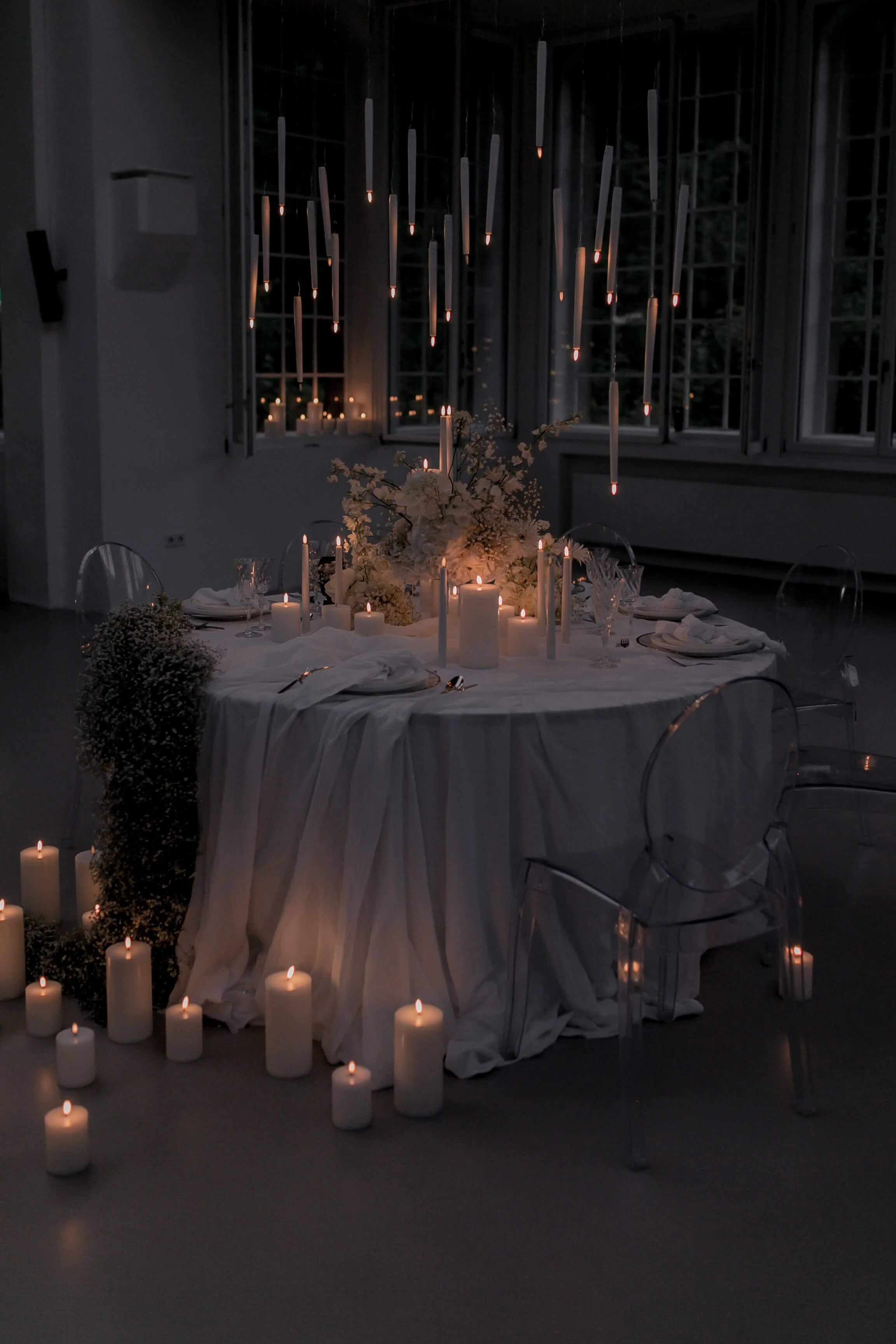 Simple wedding table decorations with candles, round table, white linen, floral centerpiece and warm ambient candlelight in a dark setting