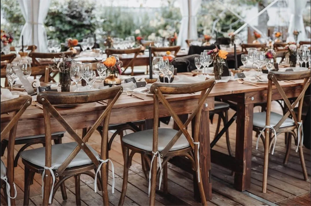 Lange Tafel mit Holztischen und Crossback-Stühlen von de Waay bei einer stilvollen Gartenhochzeit unter Zelt