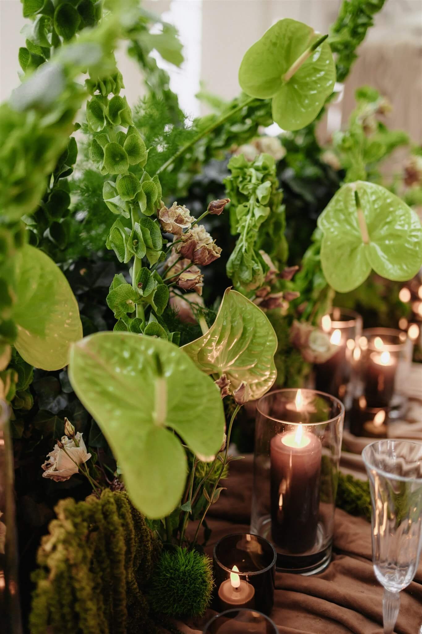 Grüne Floristik mit Salbei- und Olivtönen auf brauner Tischdecke, kombiniert mit Kerzen – natürliche Hochzeitsfarben 2026