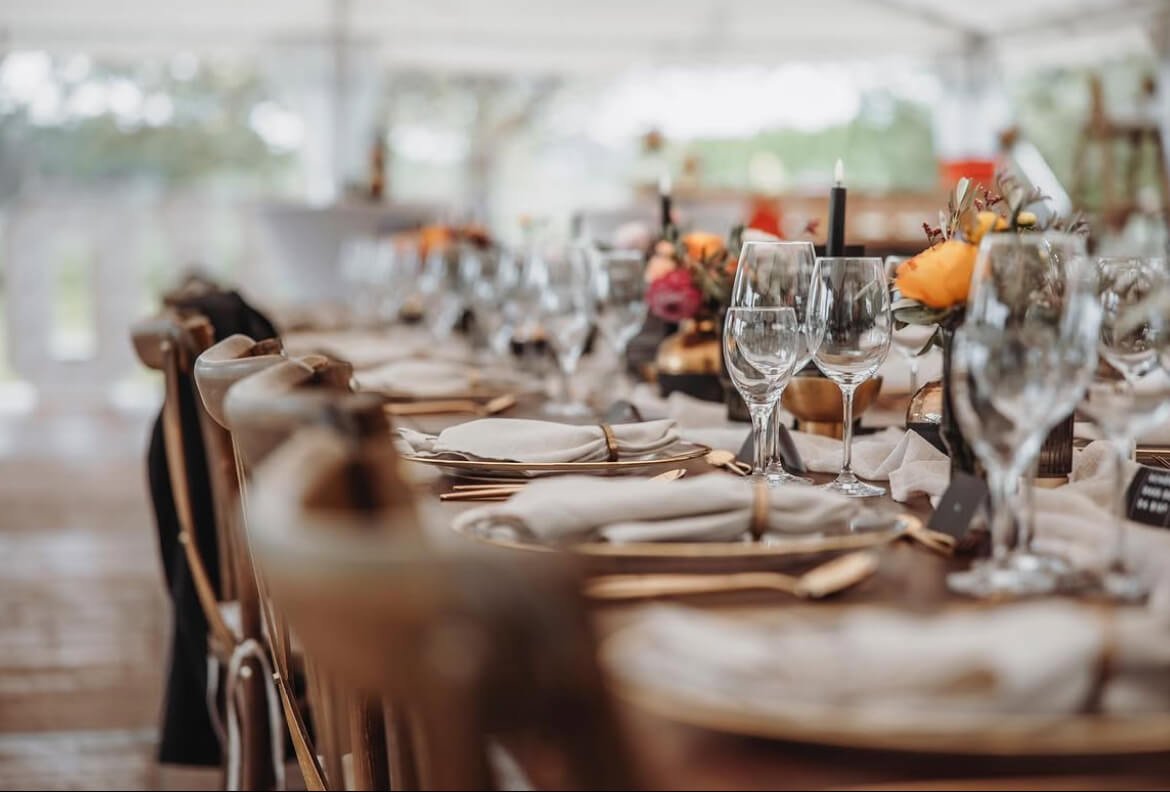 Elegantes Dinner-Setup unter Zelt bei einer Gartenhochzeit mit Holztischen und stilvollen Crossback Stühlen von de Waay