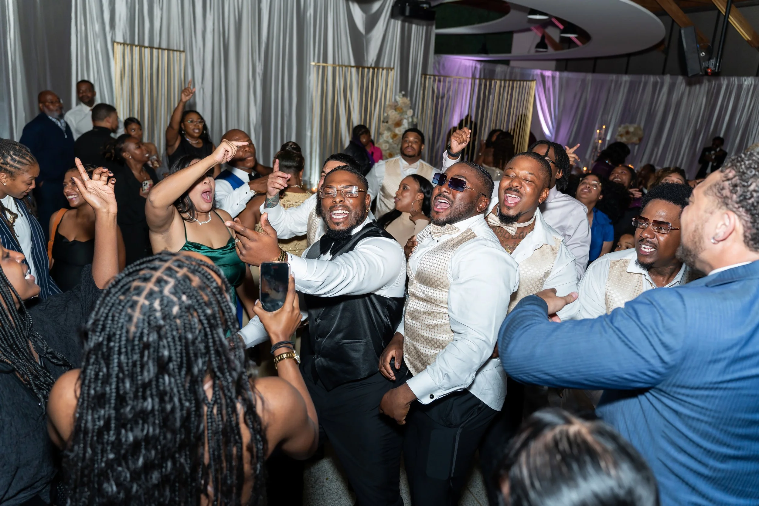 People dancing and celebrating at a party or wedding reception, with smiles and lively expressions.