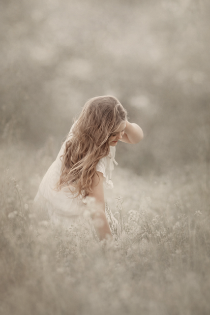 Fine art portrait of a young child standing quietly in a soft meadow, photographed in natural light with a calm, timeless feel